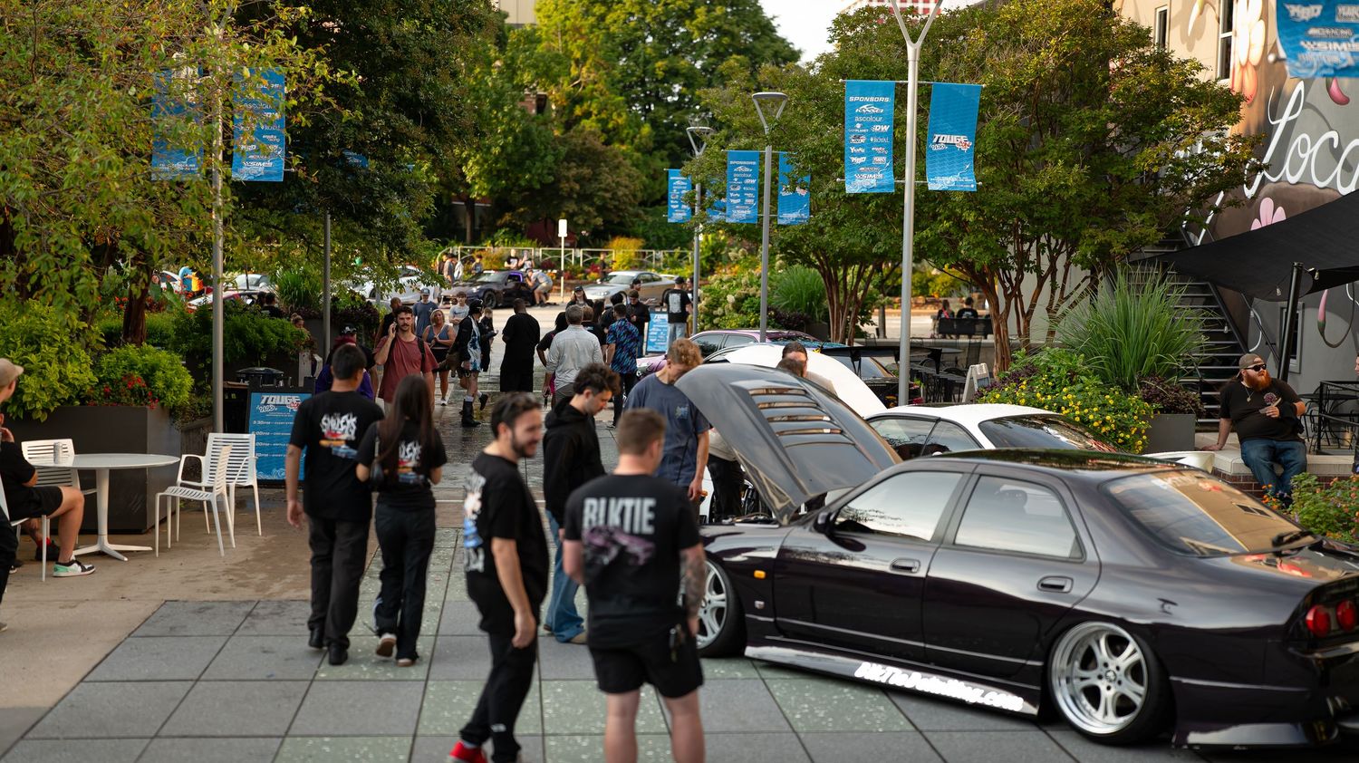 Tree-lined street view with parked cars and pedestrians on a sunny day.