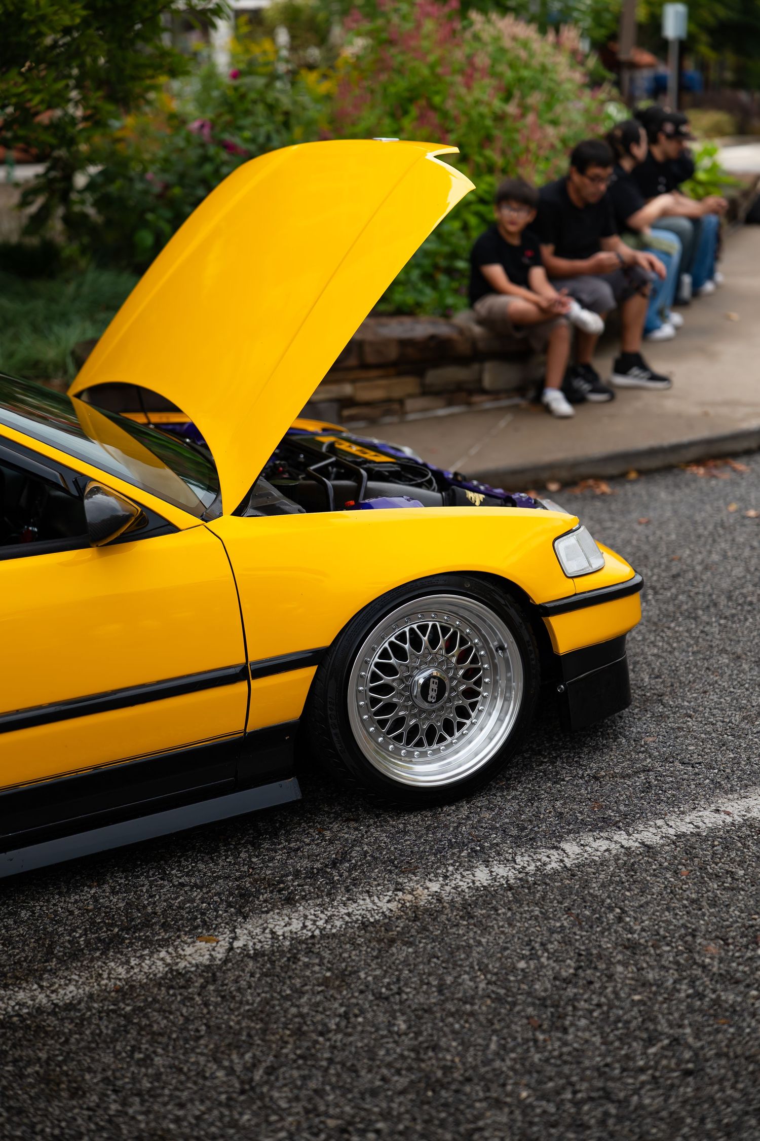 Yellow sports car with open hood showing detailed engine modifications and custom wheels.