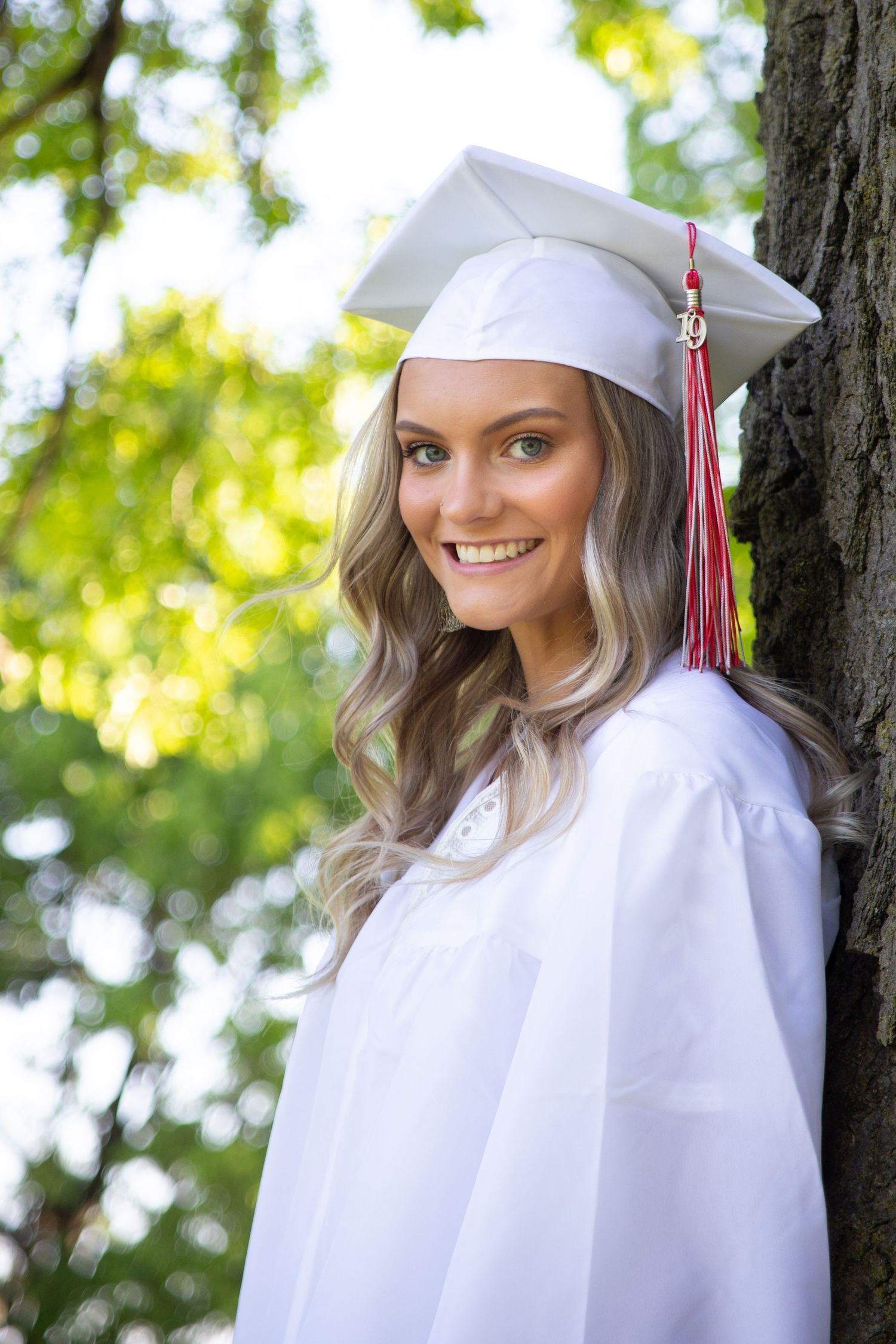 Graduate in white cap and gown smiling during outdoor portrait session.