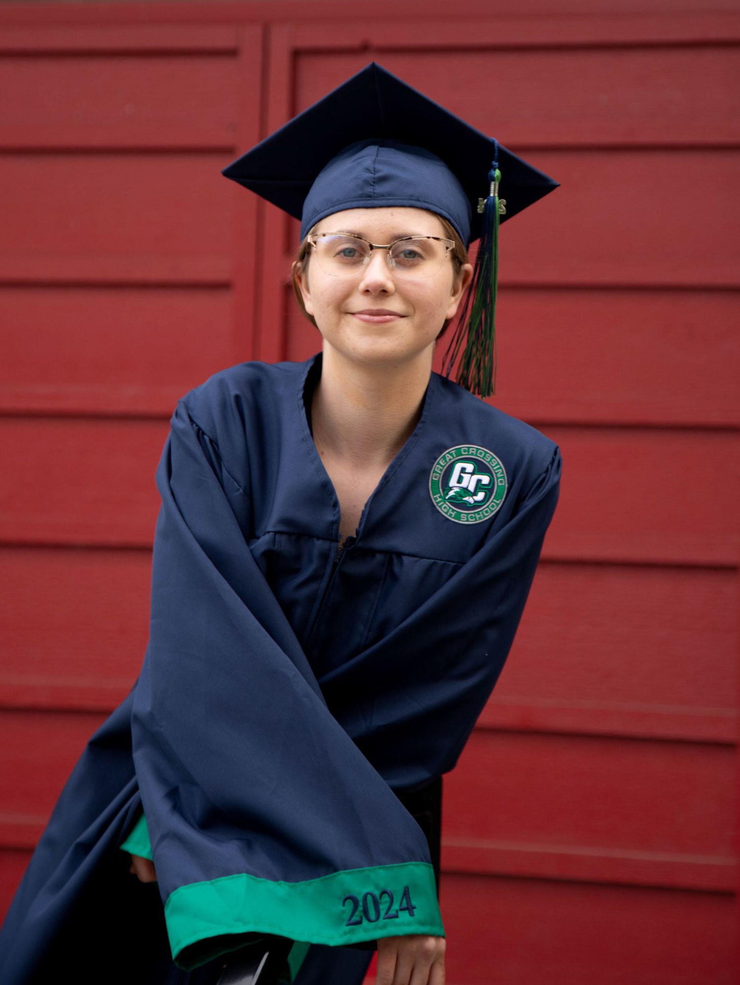 Graduate in navy blue cap and gown with green stole from class of 2022 posing outdoors.