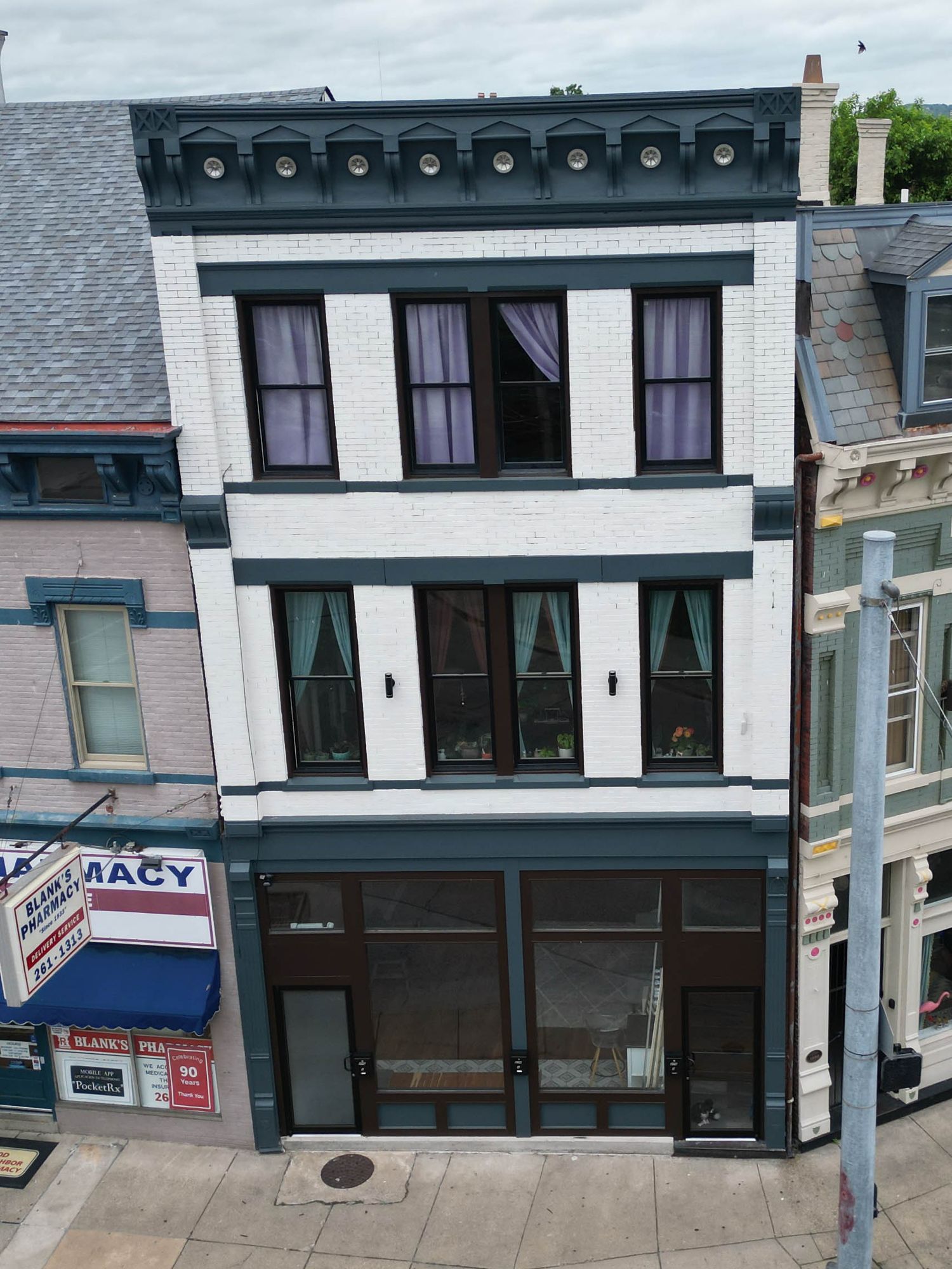 Historic three-story white commercial building with black trim and multiple windows on a city street.