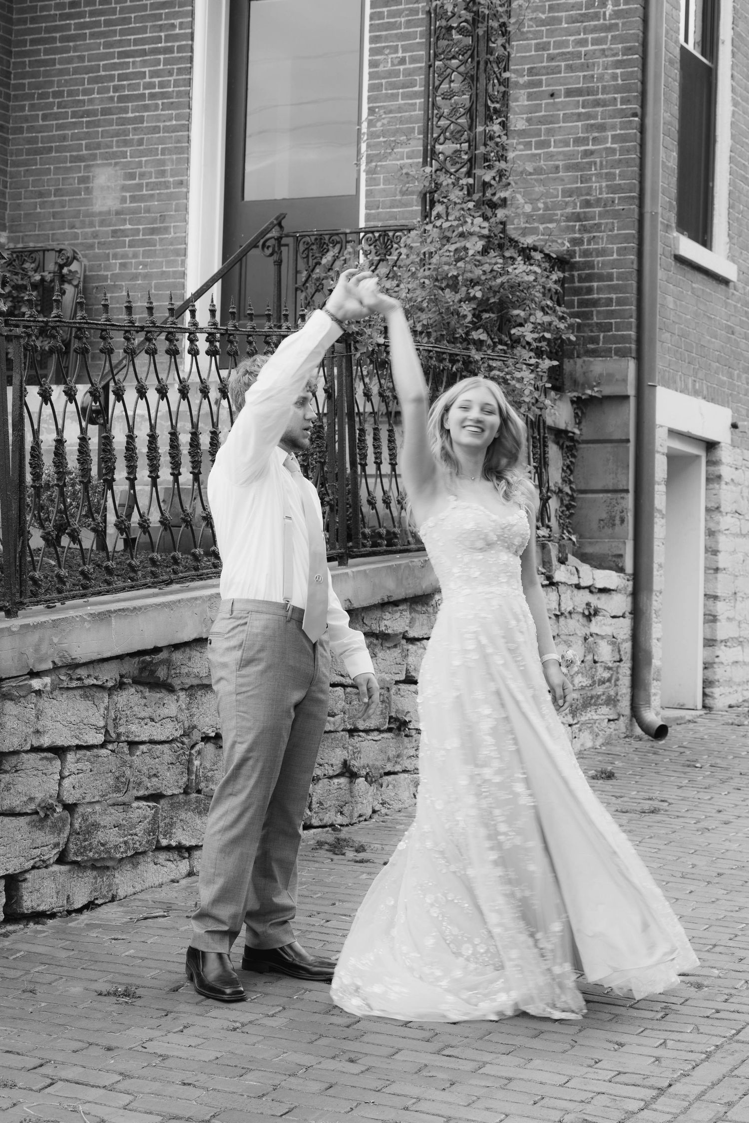 Black and white wedding photos showing couple dancing and twirling on cobblestone path.