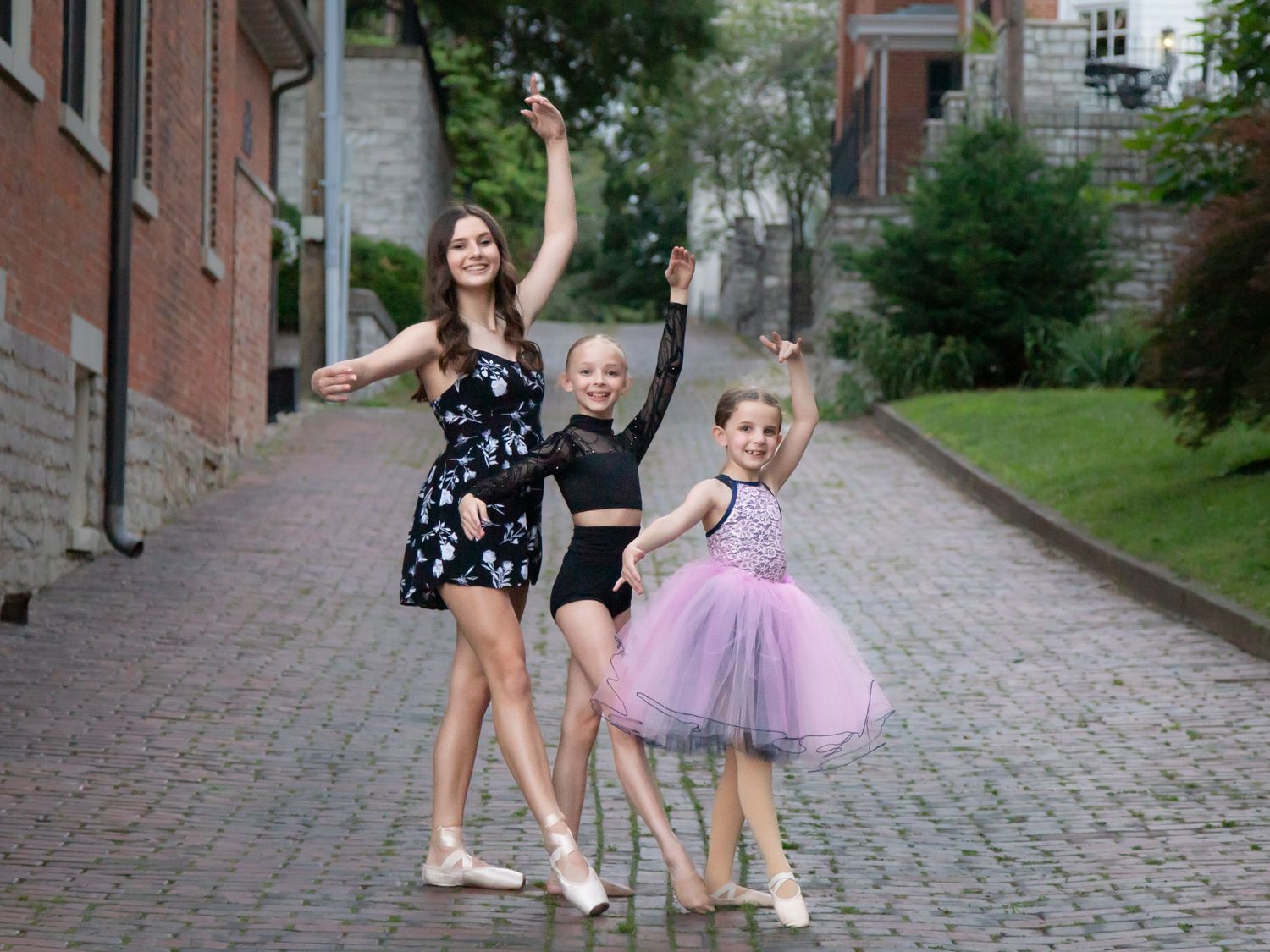 Young dancers in tutus performing on a cobblestone street.