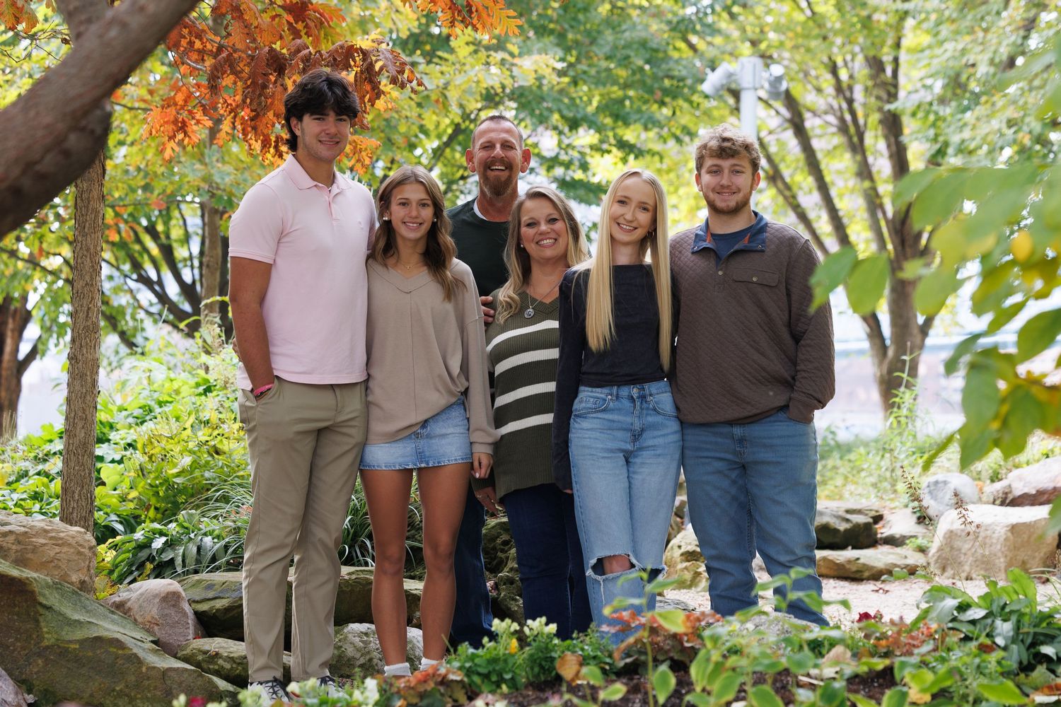 A group of people pose together in a garden setting with autumn trees and foliage in the background.
