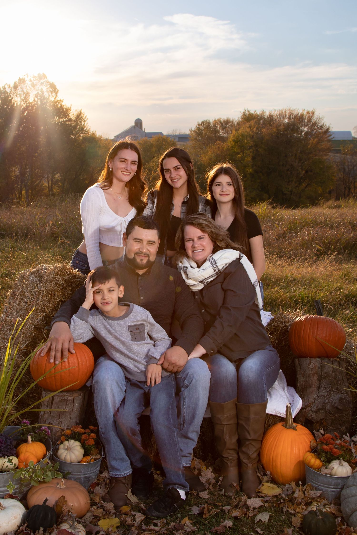 Family sitting together with pumpkins during autumn sunset photoshoot.