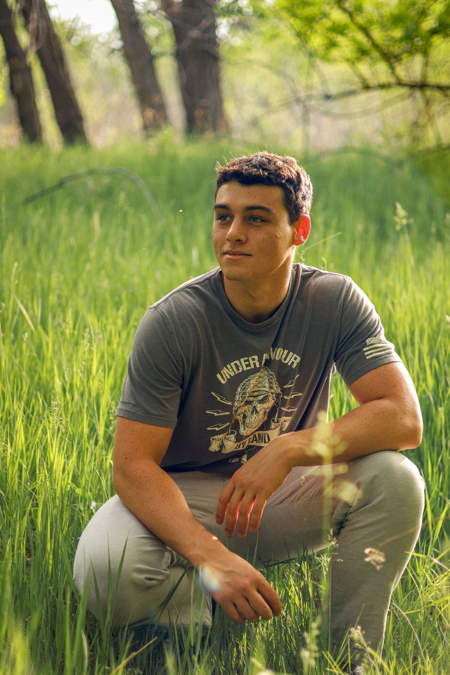 Senior photo of a boy/man looking off into the distance. Green field setting. Golden Hour.