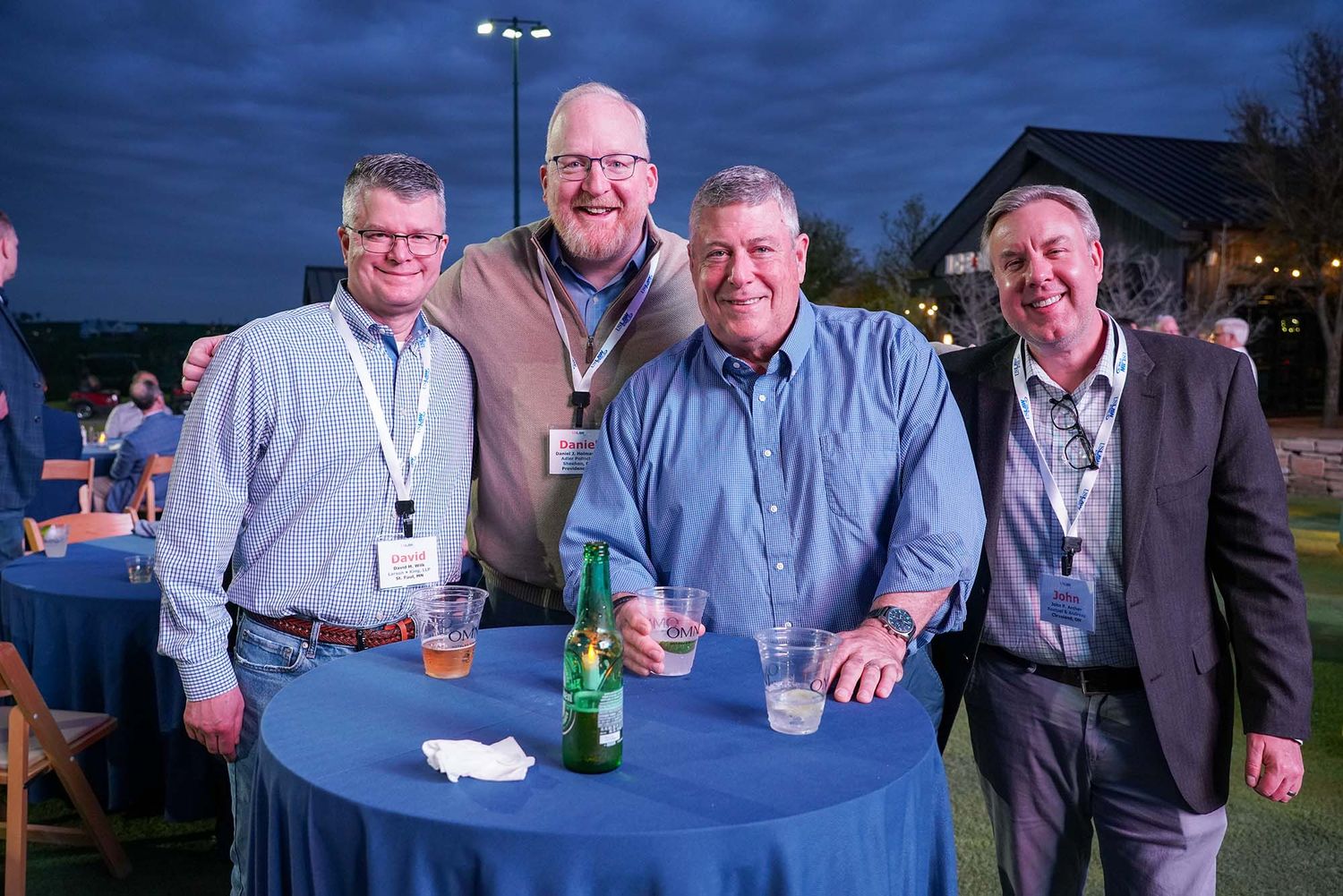 Evening networking event with professionals gathered around tables under dark blue sky.