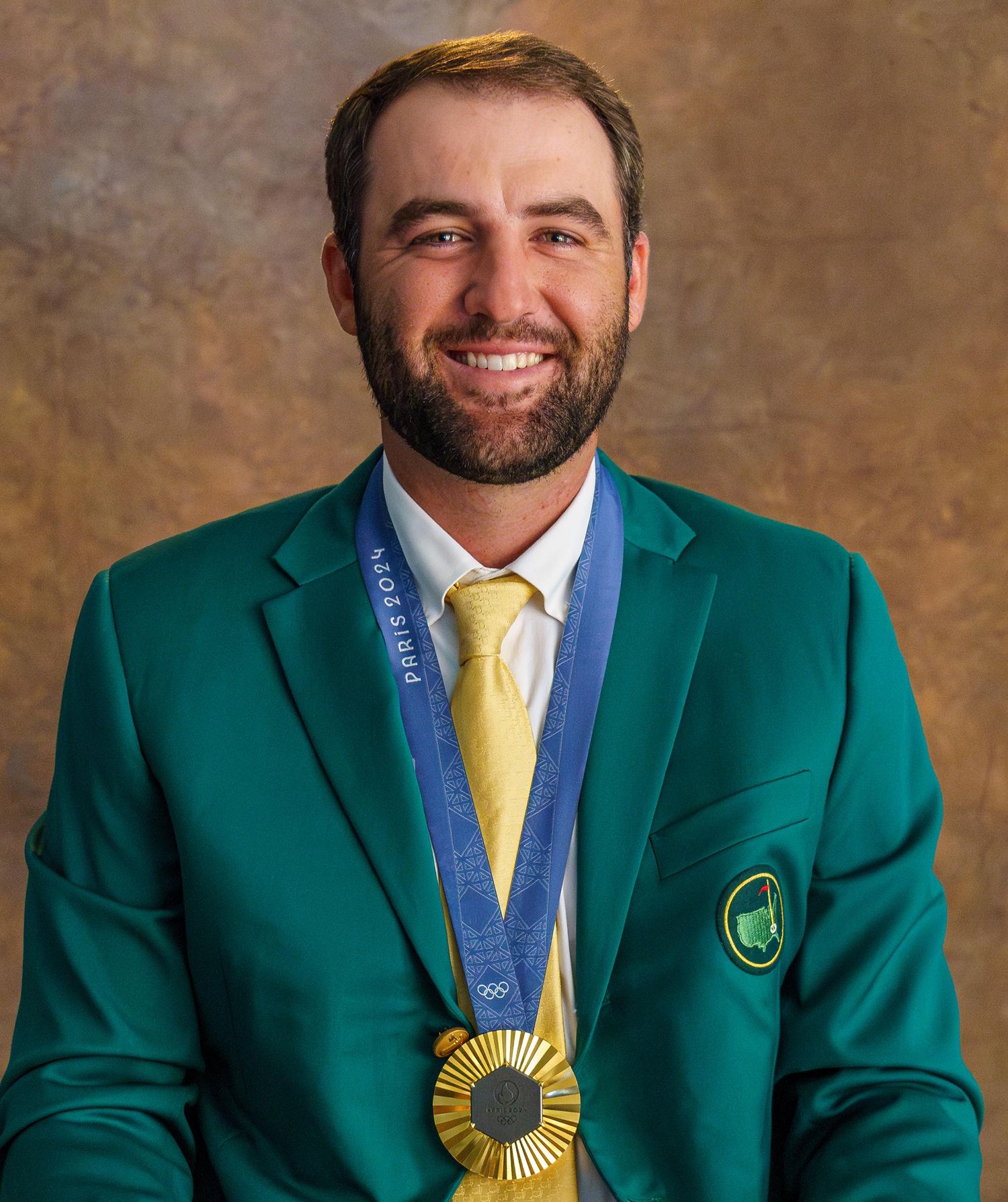 Professional golfer wearing a green Masters jacket and gold medal against brown backdrop.