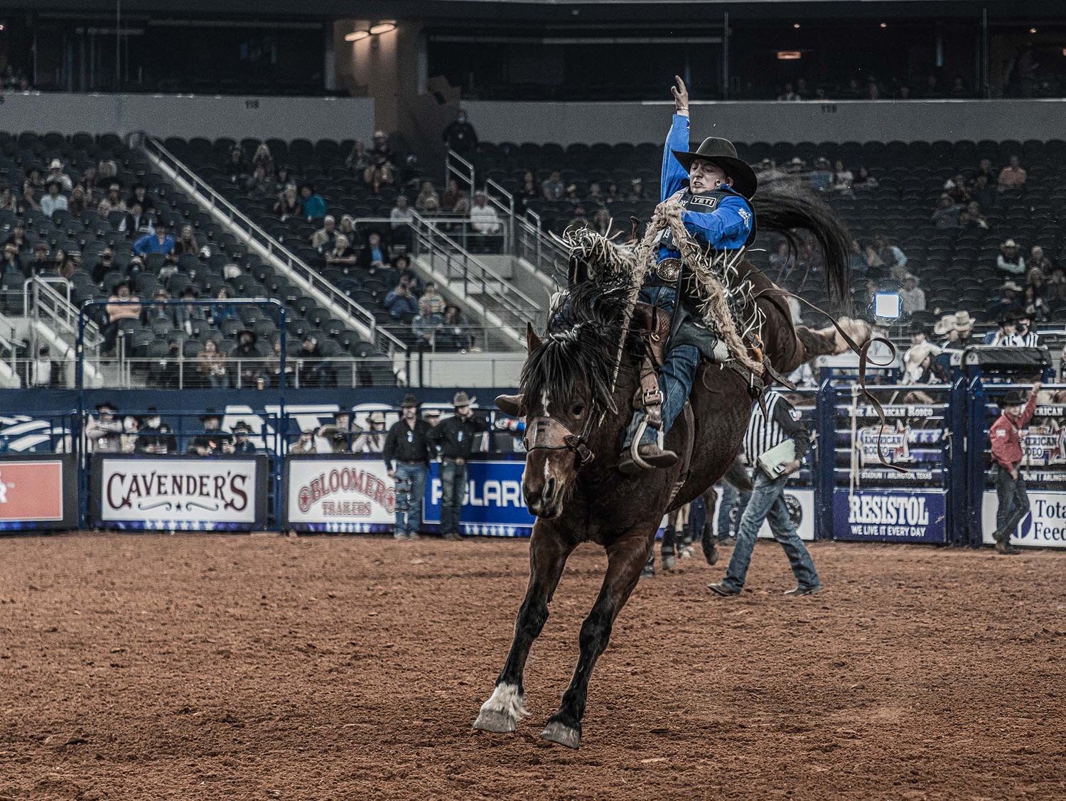 Rodeo rider performing a dramatic bronco riding stunt in an indoor arena.