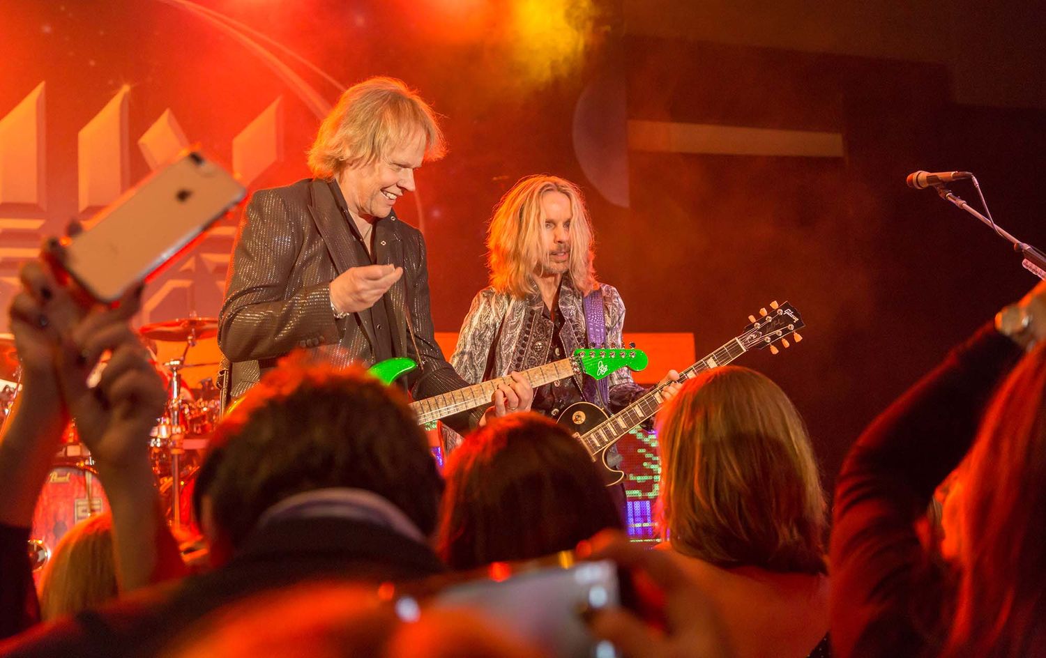 Musicians perform on stage bathed in dramatic red and orange lighting during a live concert.