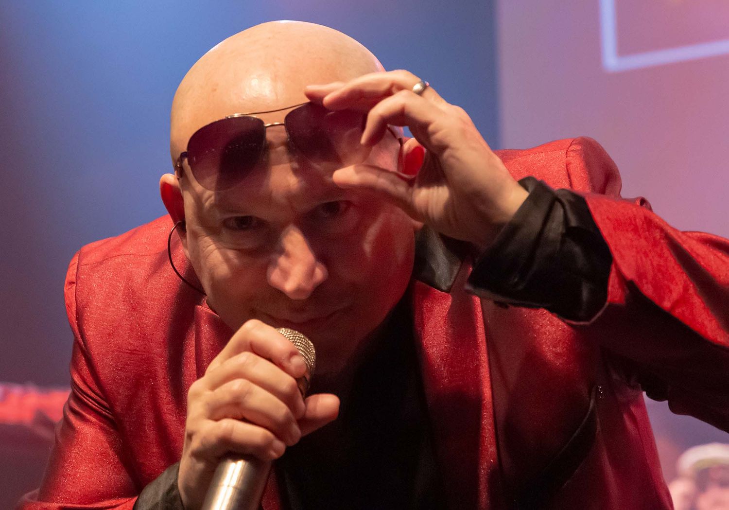 Musicians in red suits perform on stage with dramatic lighting and instruments.