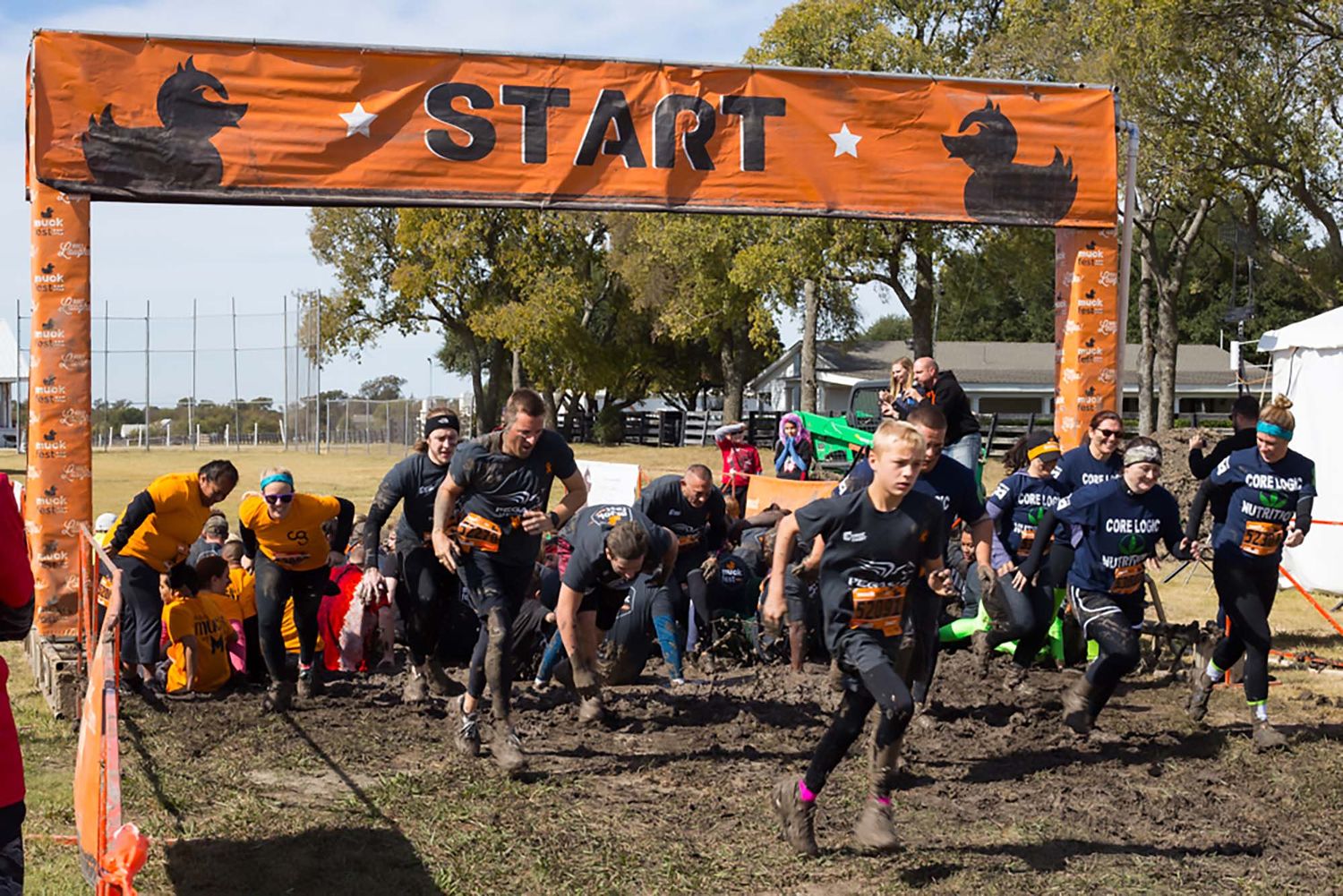 Outdoor obstacle course race with orange 'START' banner and participants gathering at the starting line.