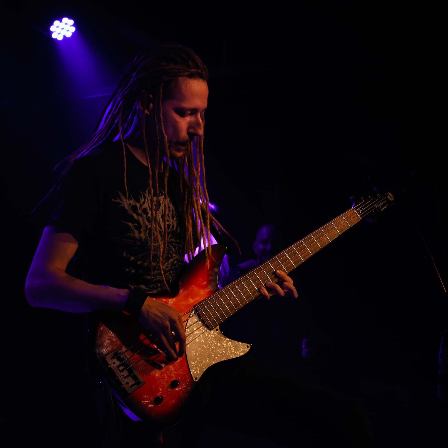 Guitarist plays electric guitar in dark lighting with purple stage effects.