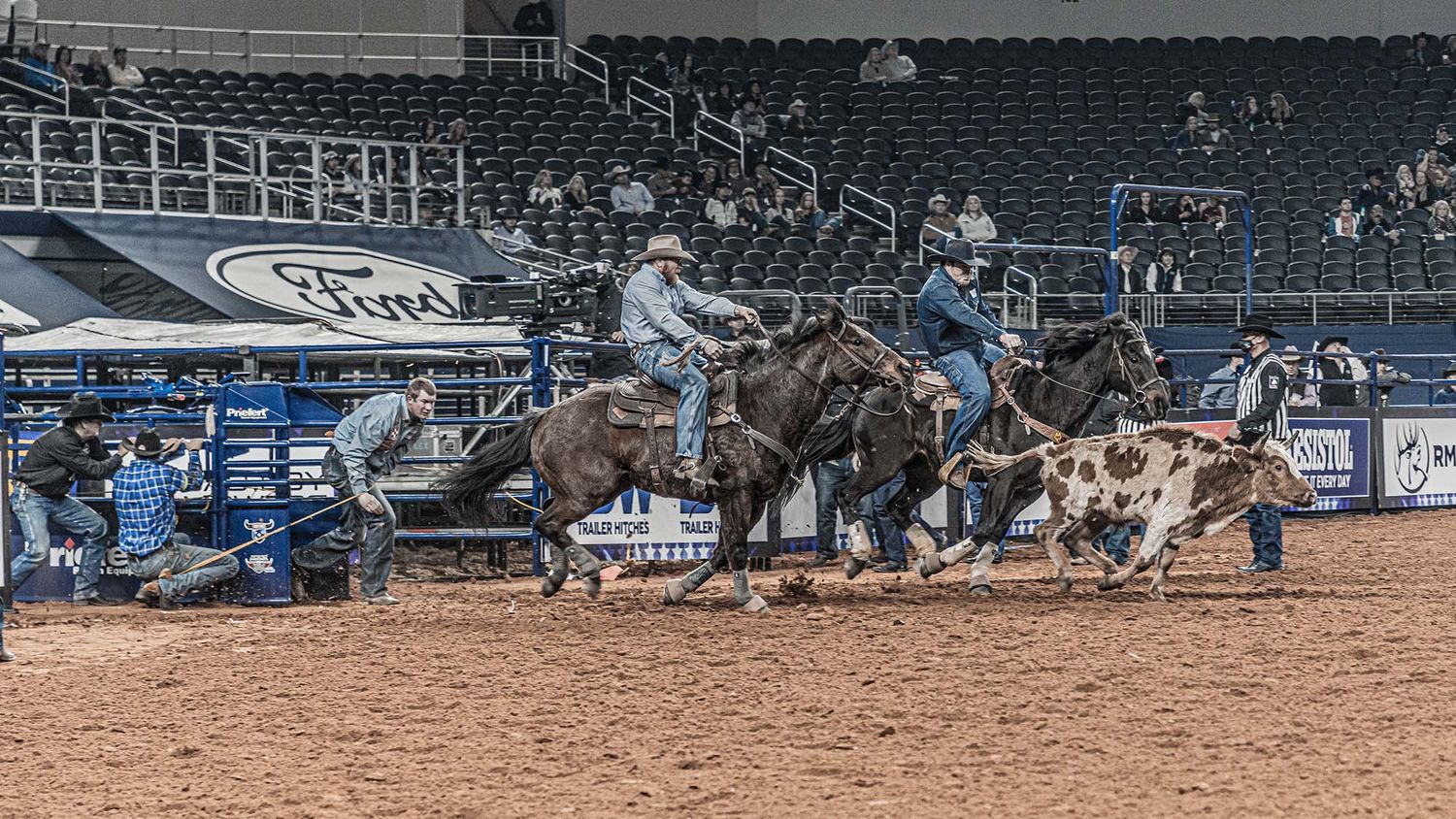 Wide view of a rodeo arena with stadium seating and dirt floor.