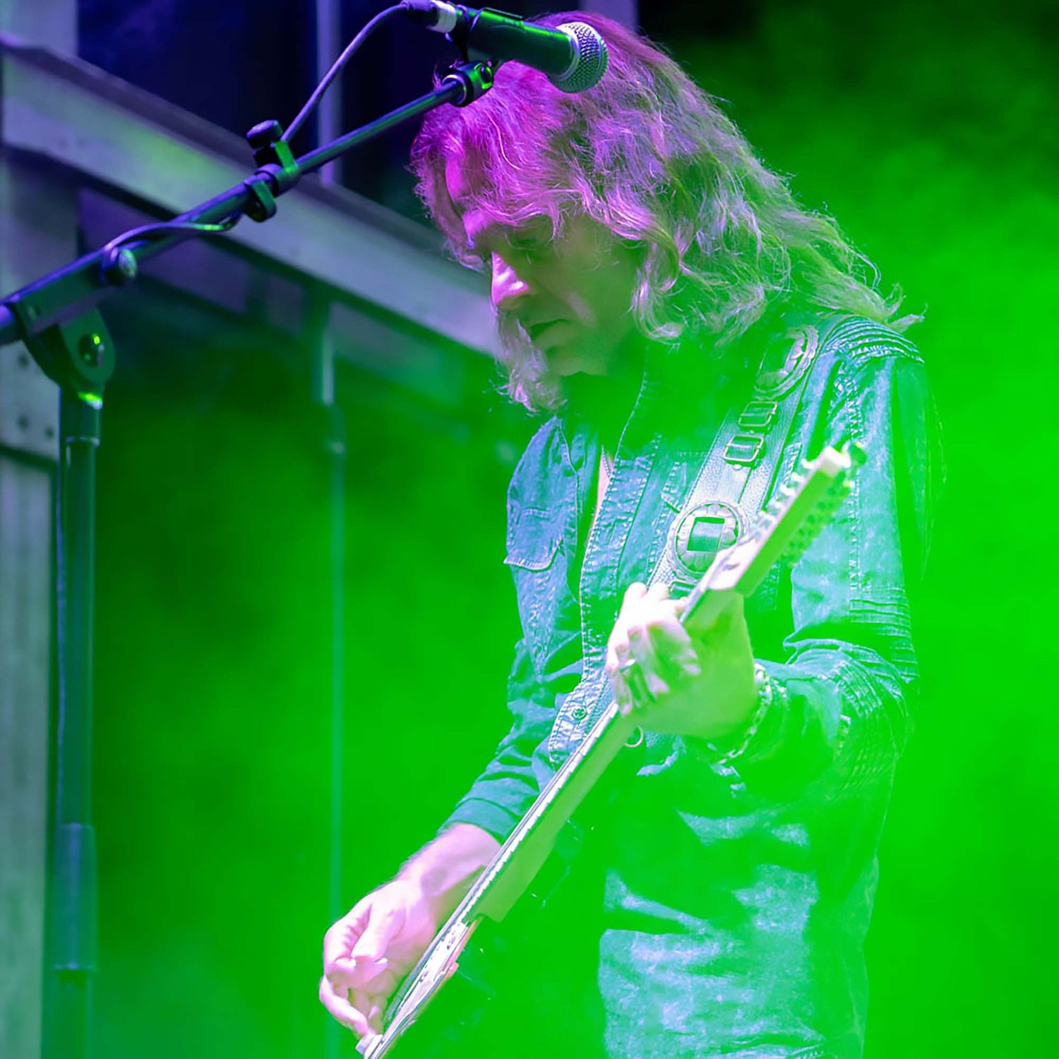 Guitarist performing under intense green stage lighting with dramatic motion blur effects.