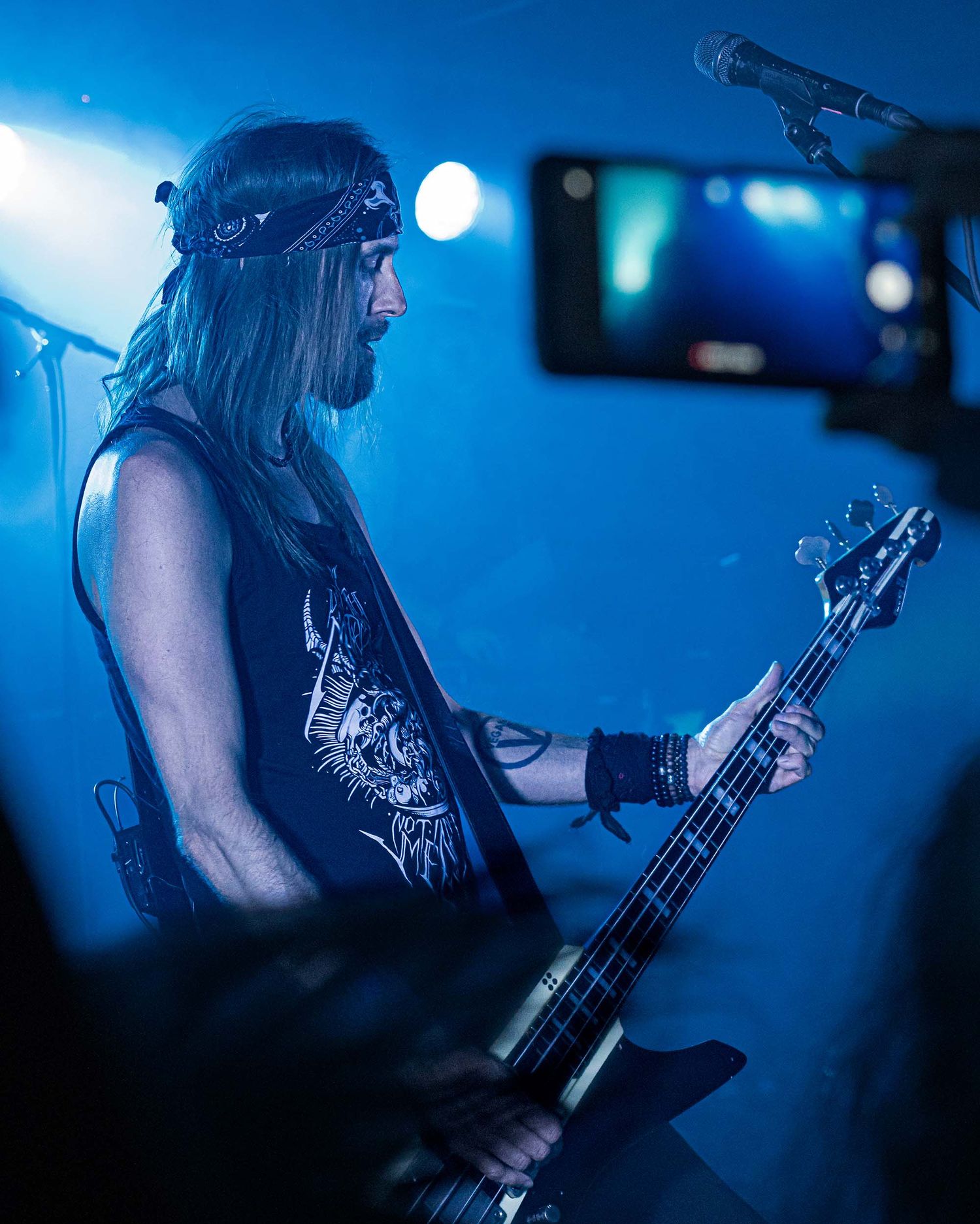 Concert performance in blue lighting showing a musician playing bass guitar on stage.