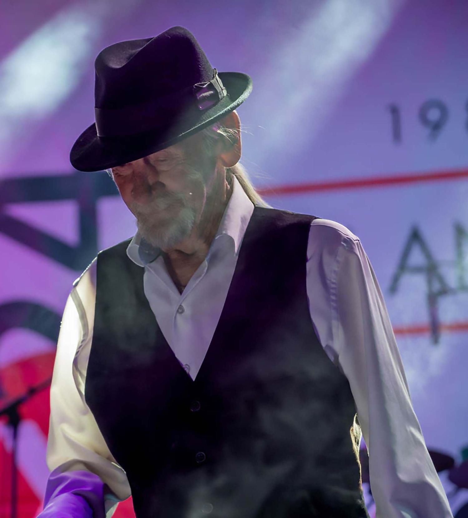 Performer in black vest and cap on stage with purple lighting effects.