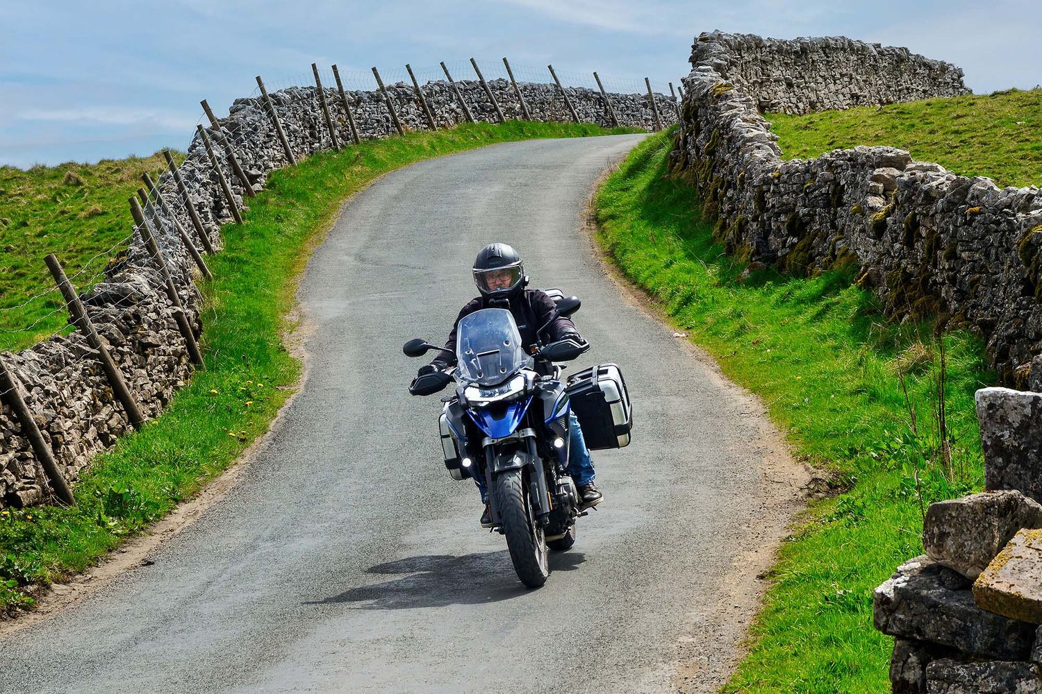 Motorcycles riding along a winding country road bordered by stone walls.