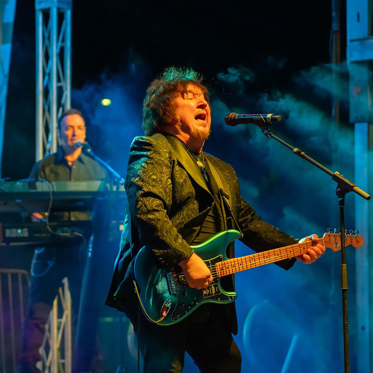 Musicians performing under blue stage lighting with guitars and microphones.