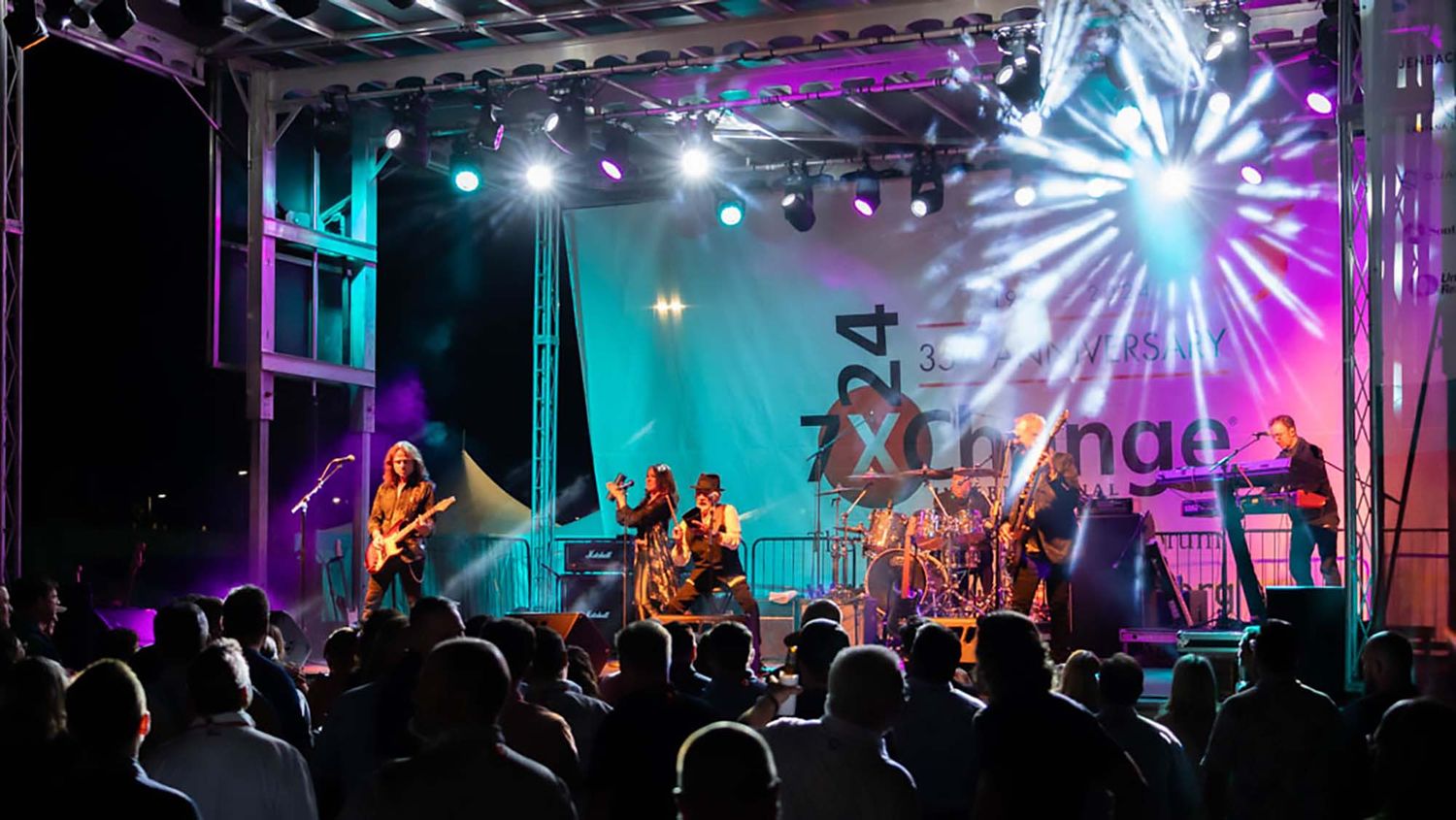 Wide concert venue shot with colorful lighting effects and starburst patterns on stage.