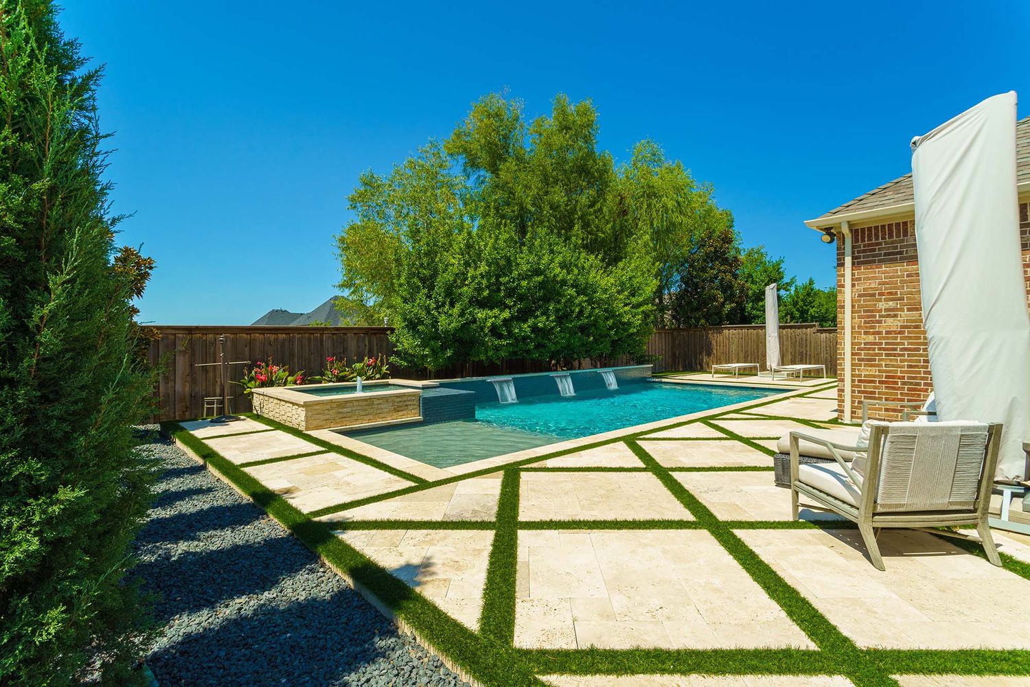 Expansive backyard patio with swimming pool and lush green landscaping under bright blue sky.