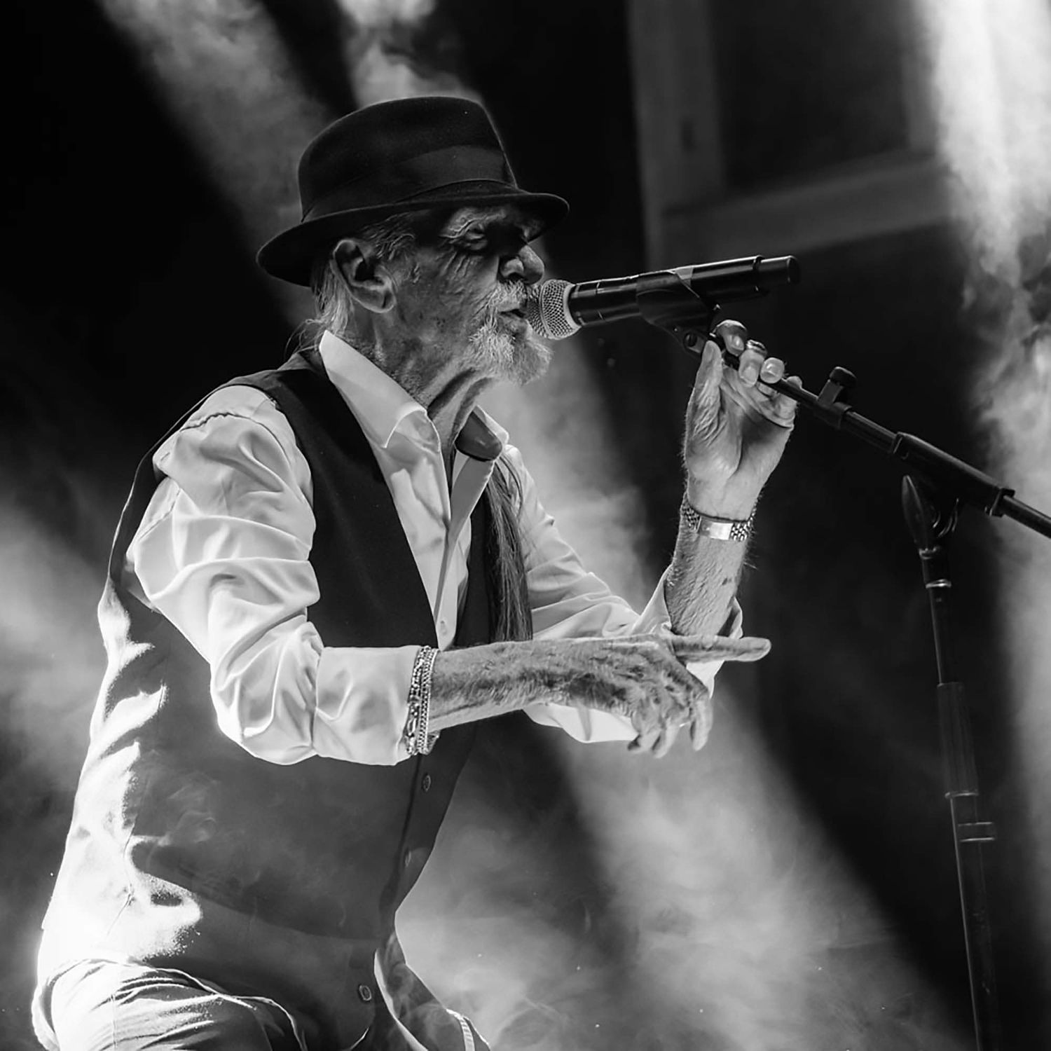 Performer in white clothing silhouetted against atmospheric stage smoke during live performance.