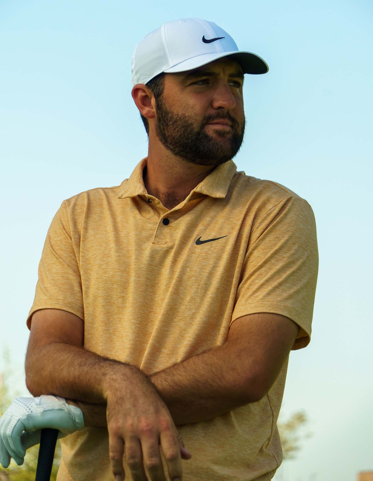 Golfer in yellow polo and white cap relaxing outdoors on sunny day.