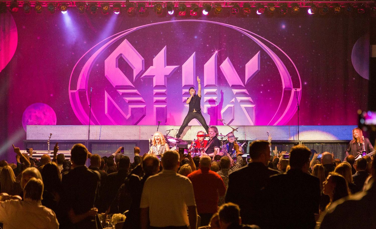 Concert stage with pink and purple lighting effects and crowd silhouettes visible.