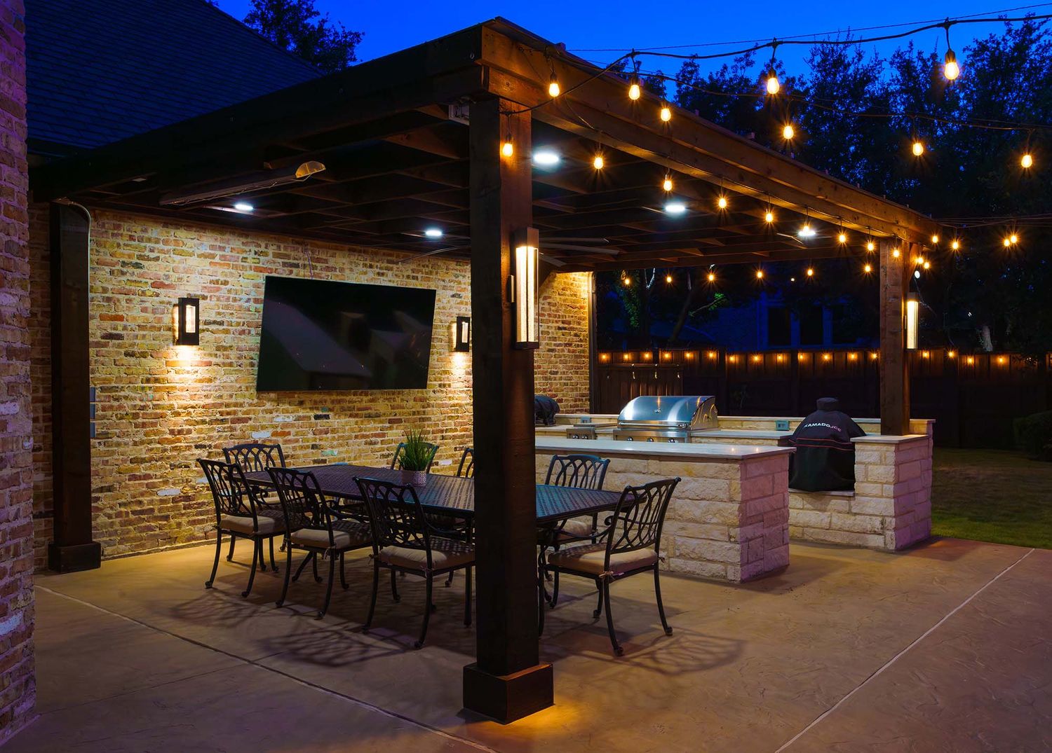 Stone patio with bistro lights strung overhead and outdoor dining furniture at dusk.