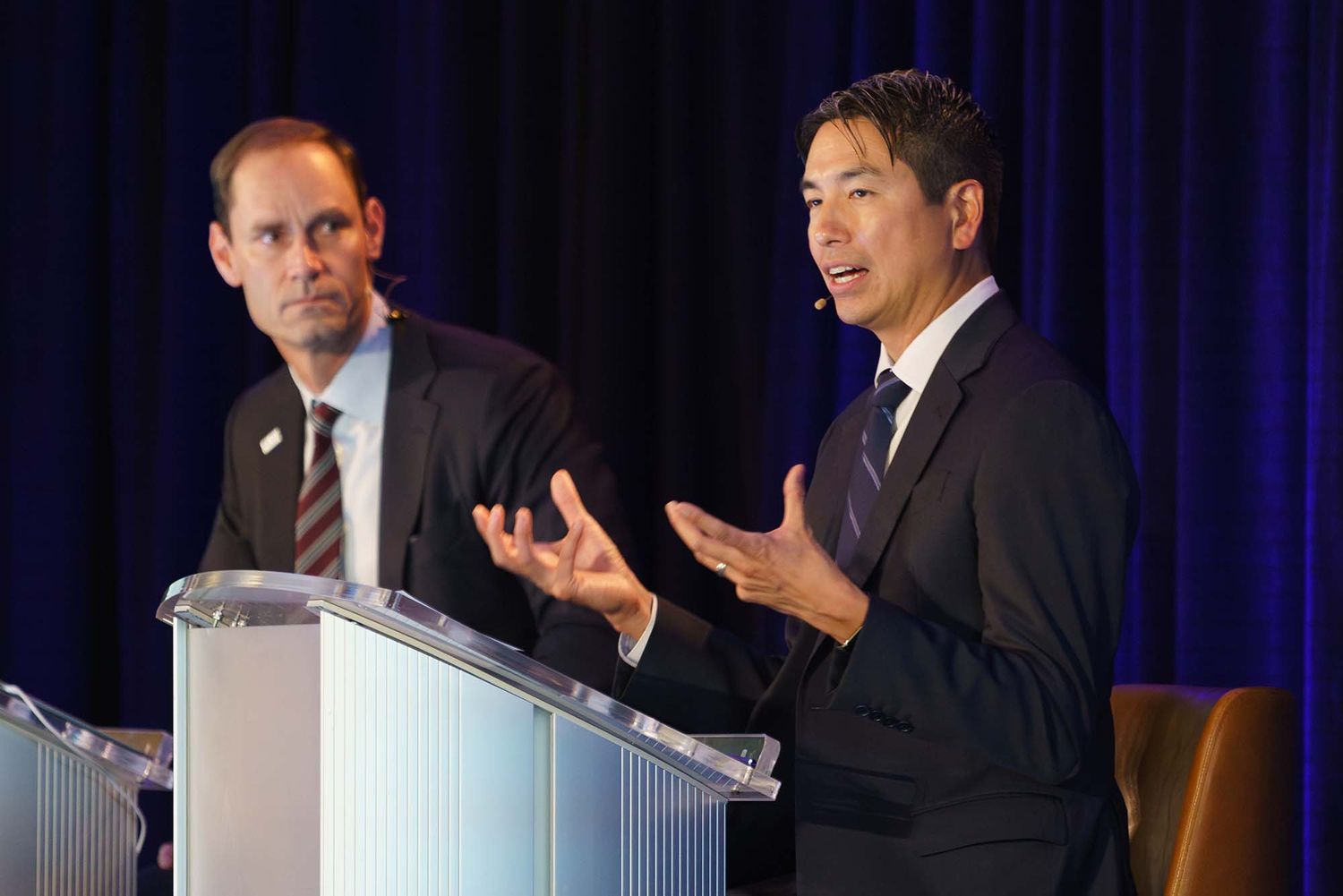 Speakers at a professional conference on stage with blue curtain backdrop.