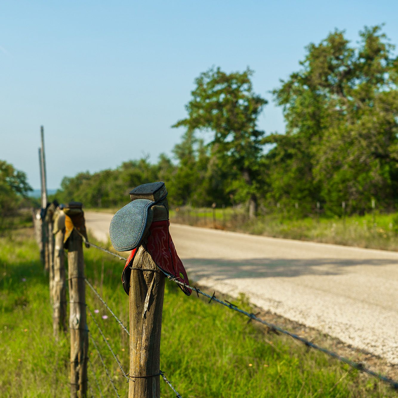 Rustic wooden fence posts with boots placed on top along a country road.