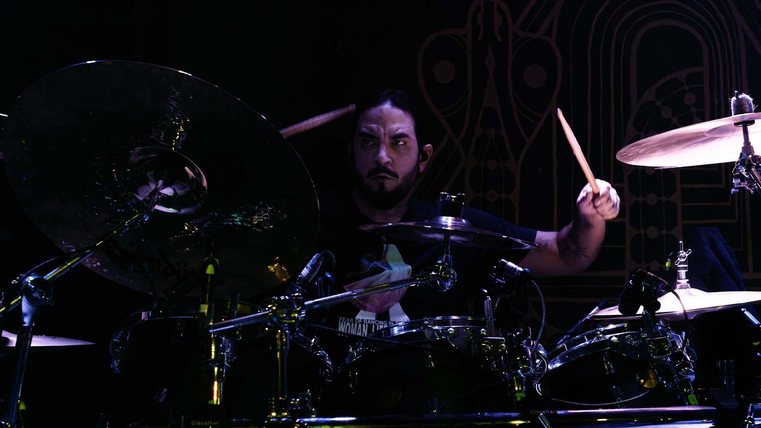 Drummer performs on dark stage with dramatic lighting effects.
