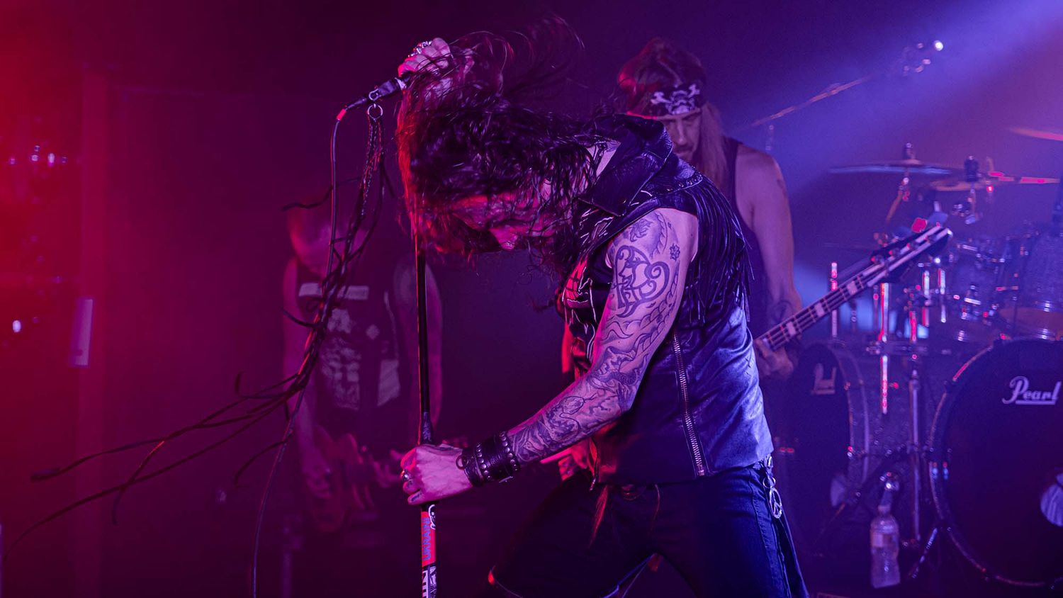 Concert stage illuminated with purple lighting as performers play instruments during an energetic live show.