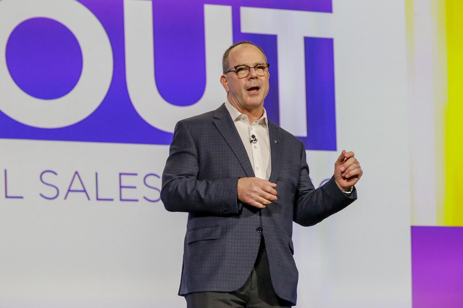 Business speaker giving animated presentation on stage with bright backdrop.