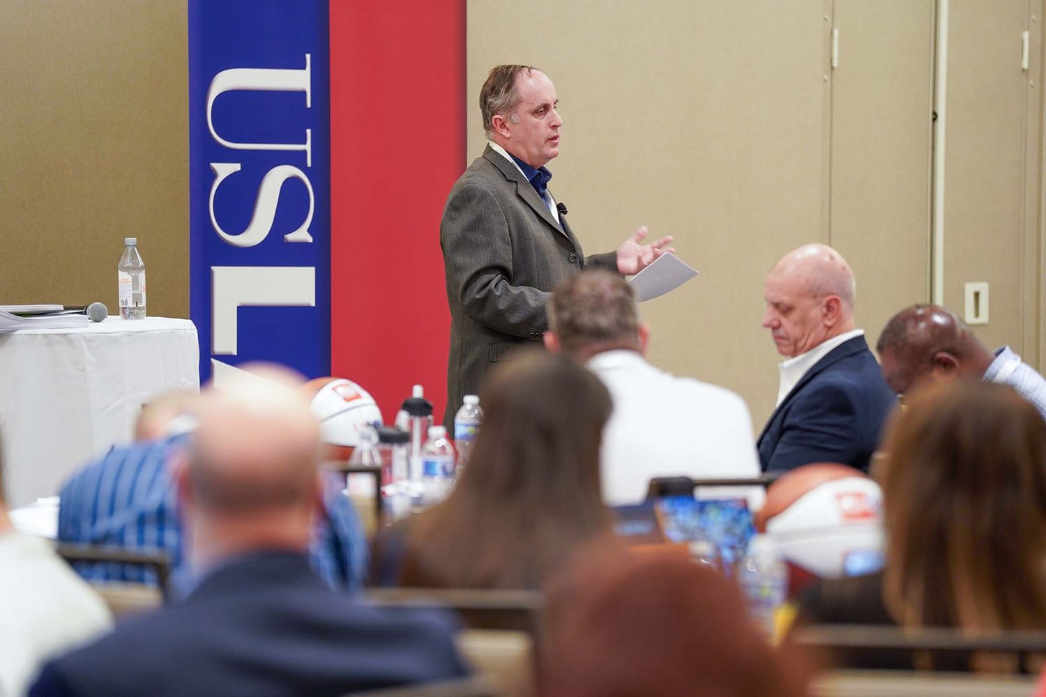 Professional conference setting with red and blue branded banners visible.