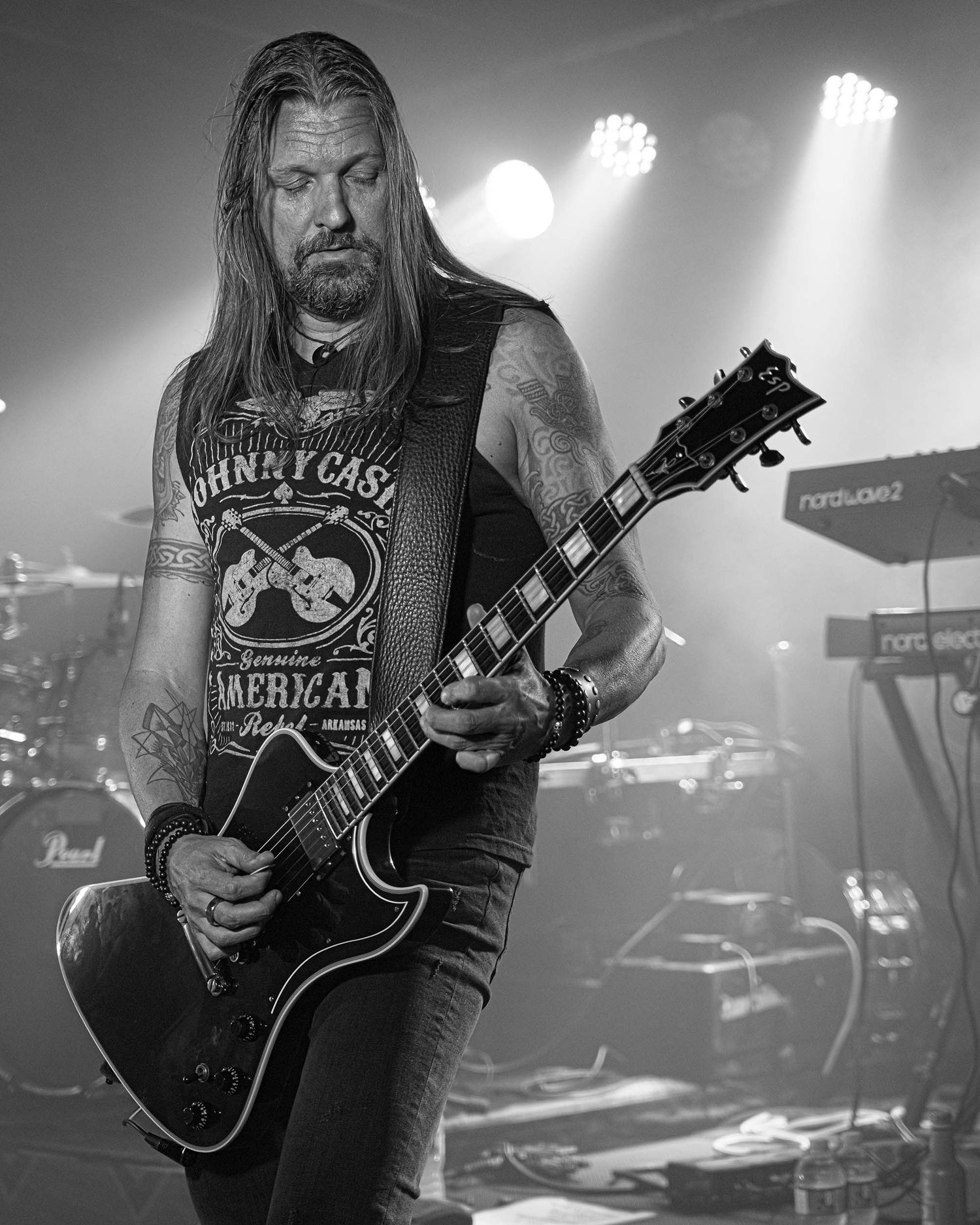 Musicians playing electric guitars on stage with dramatic lighting and equipment visible in background.
