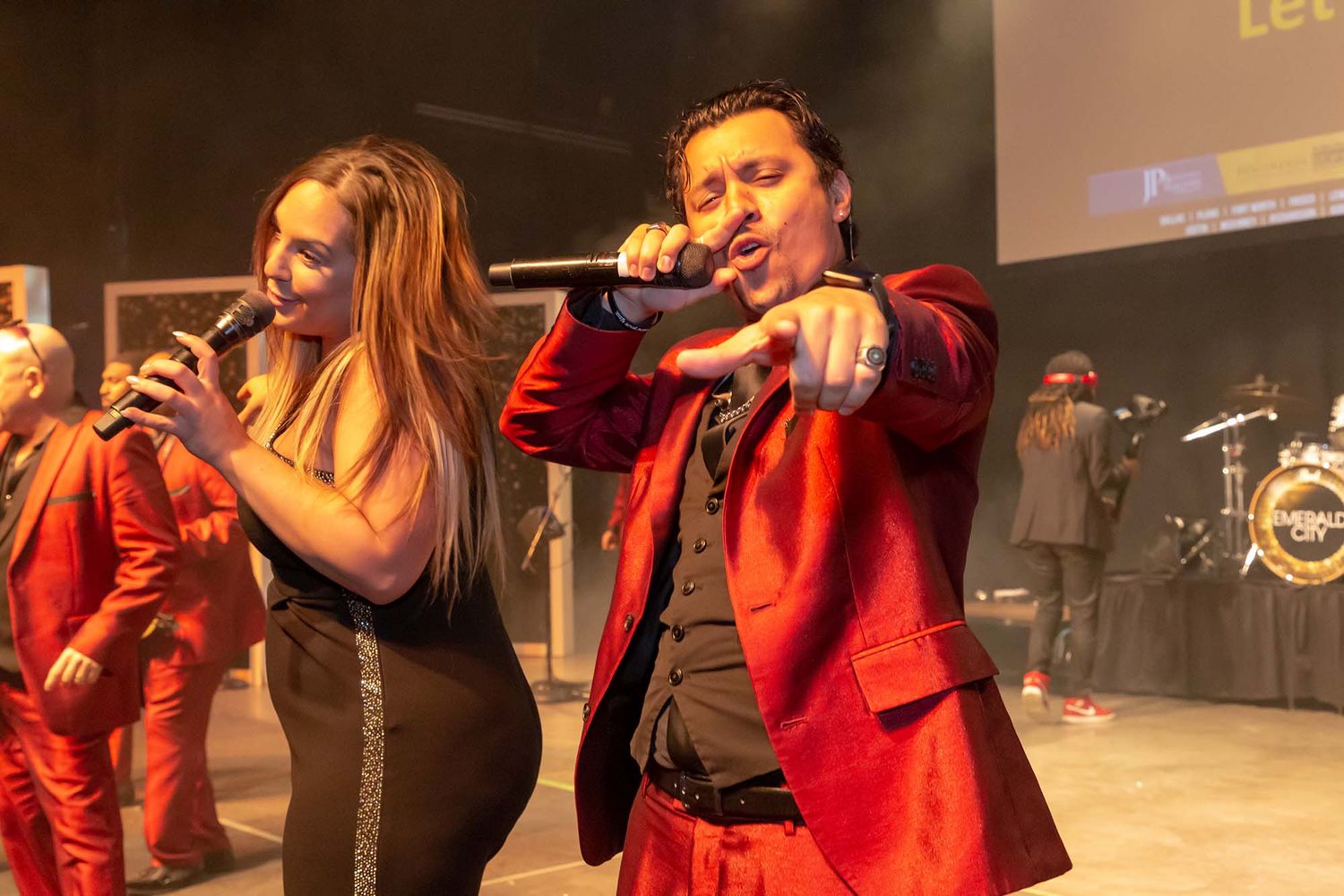 Performers in red outfits singing on stage during an indoor concert performance.