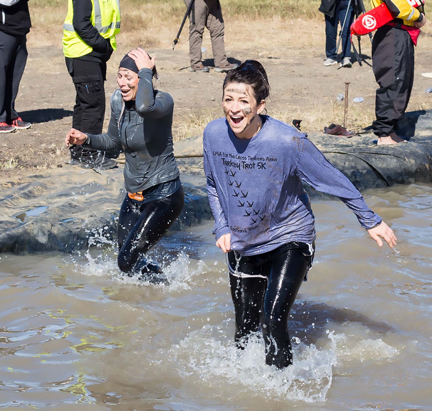 Children running and splashing through muddy water during an outdoor obstacle course event.