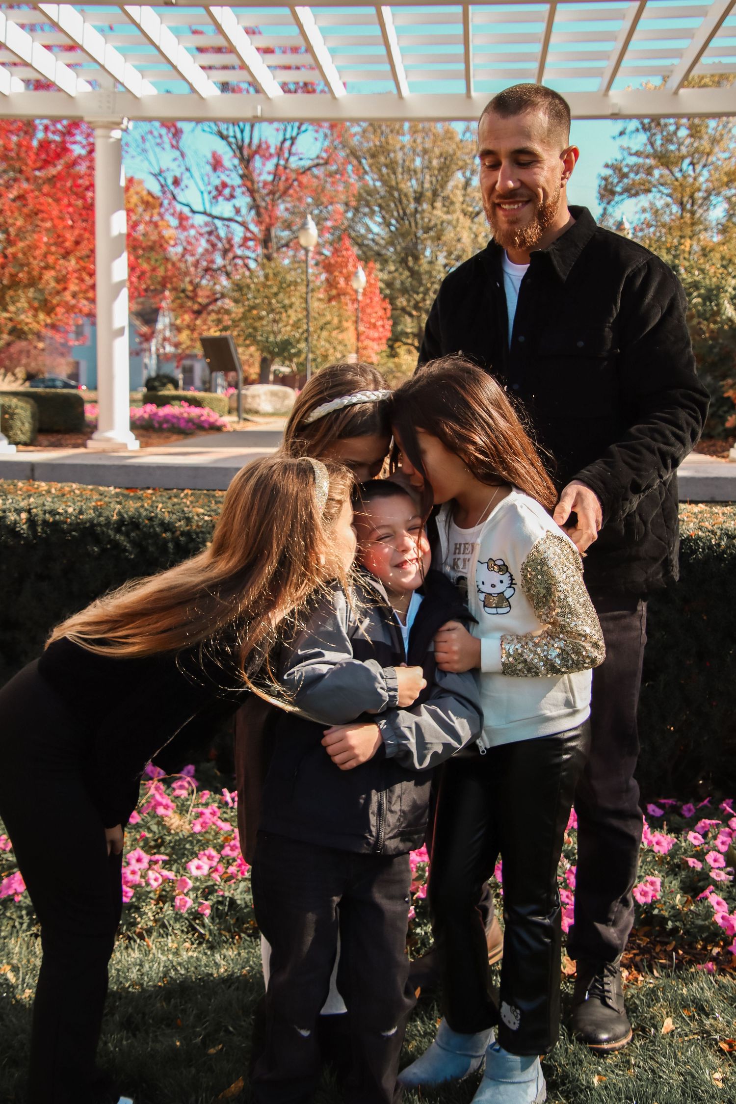 Dad smiling as sisters give brother a kiss.