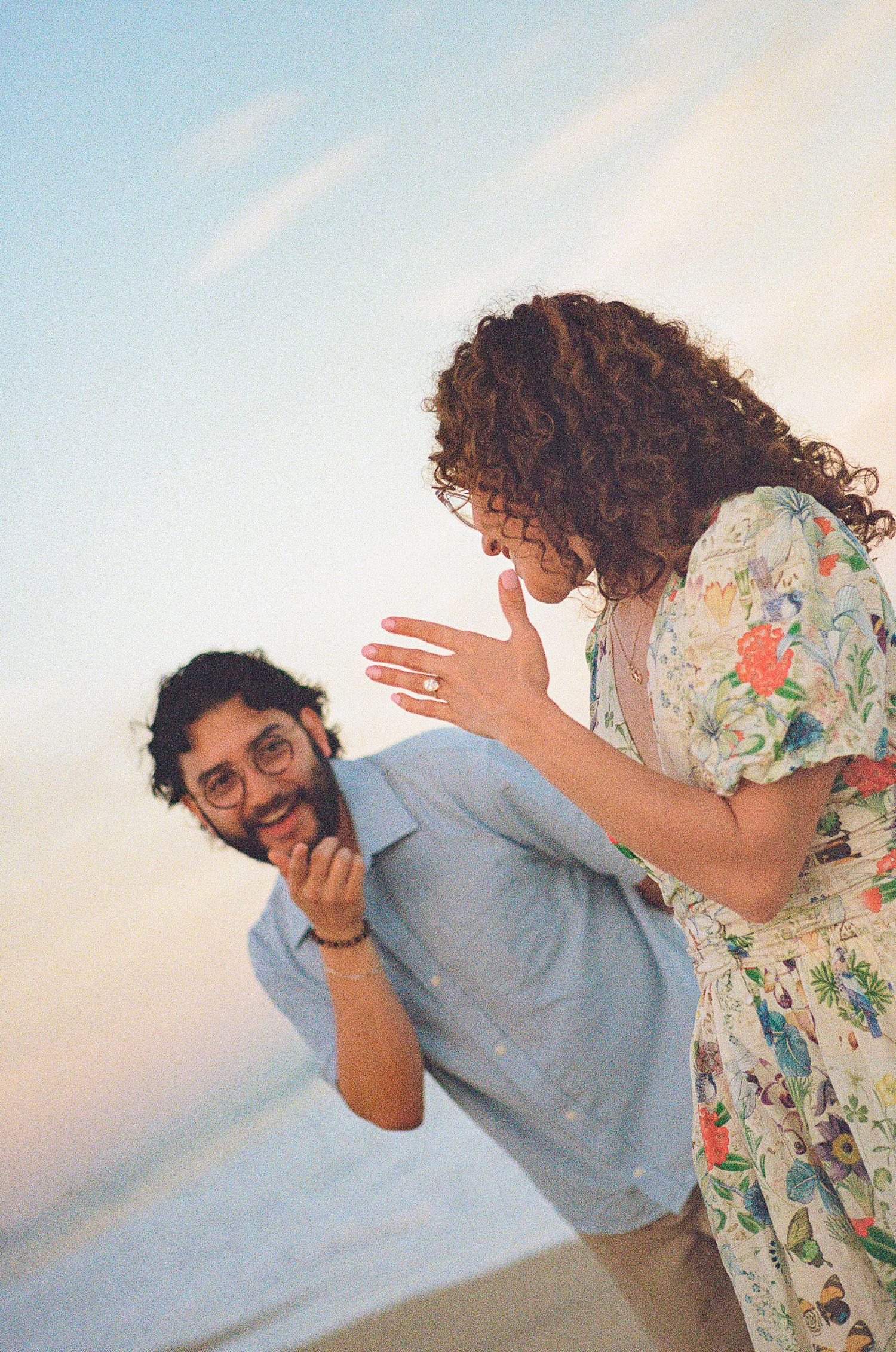 Couple celebrating engagement on beach at sunset, woman showing off ring while man smiles joyfully in San José del Cabo.