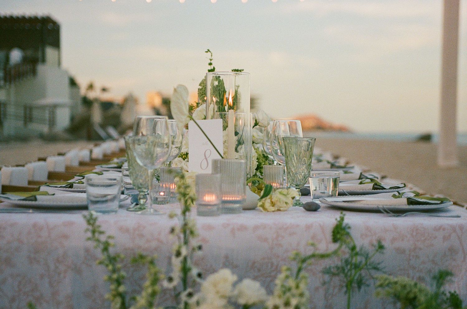 Soft and romantic wedding reception table with green florals and glassware.