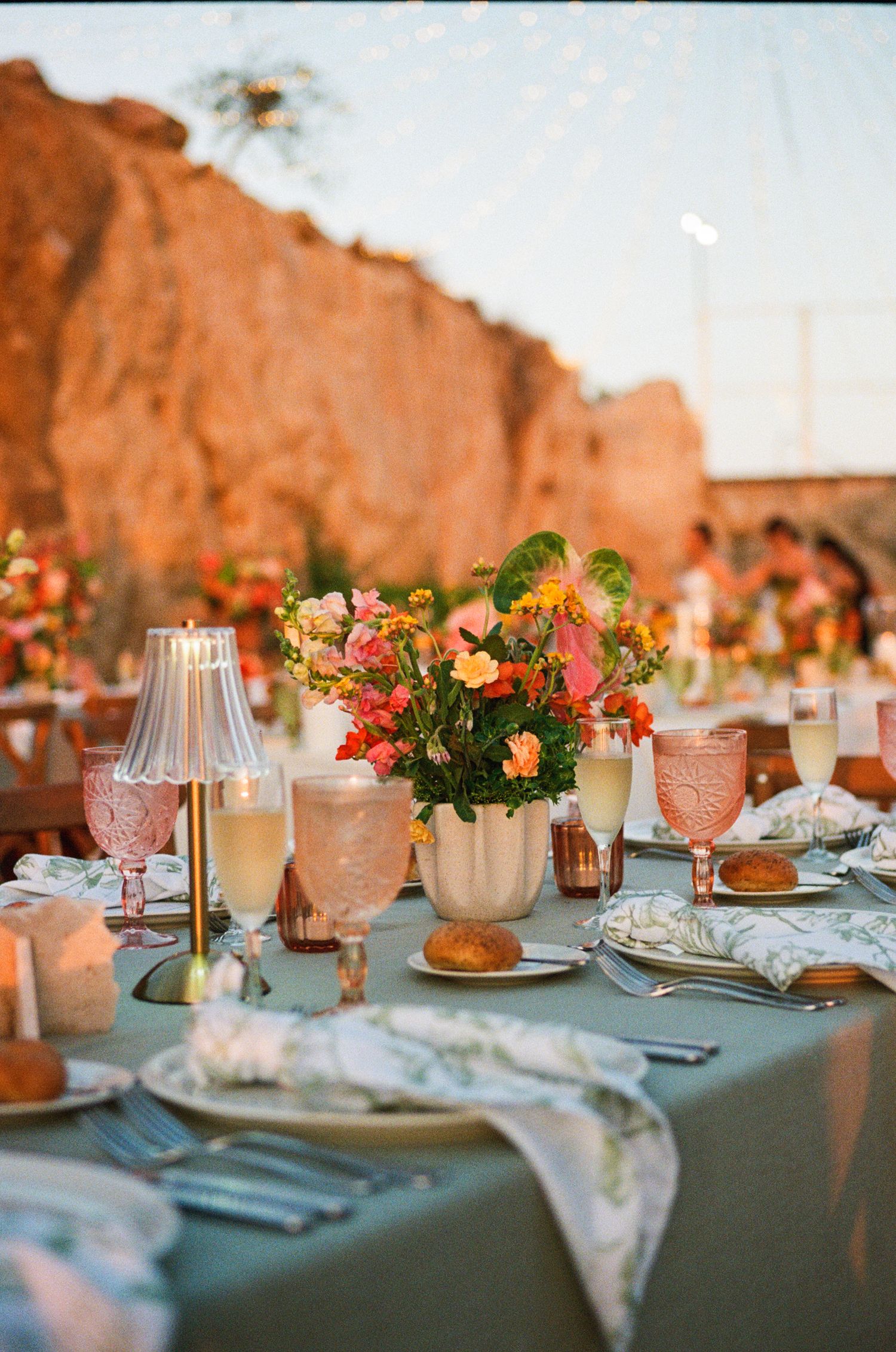 Vibrant and colorful wedding reception table with lots of warm flowers and glassware.