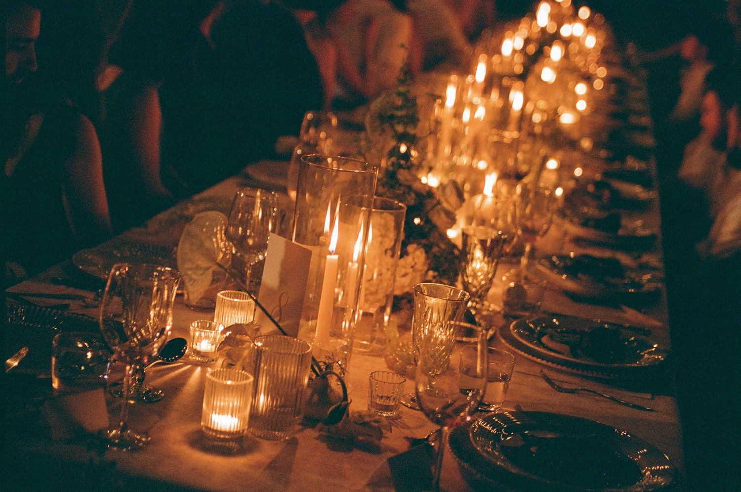 Romantic candlelit wedding reception table with warm floral details and glassware on 35mm film.