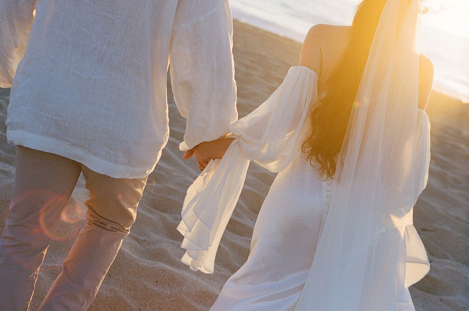 Newly eloped couple holding hands running off into the sunset on beach near Todos Santos.