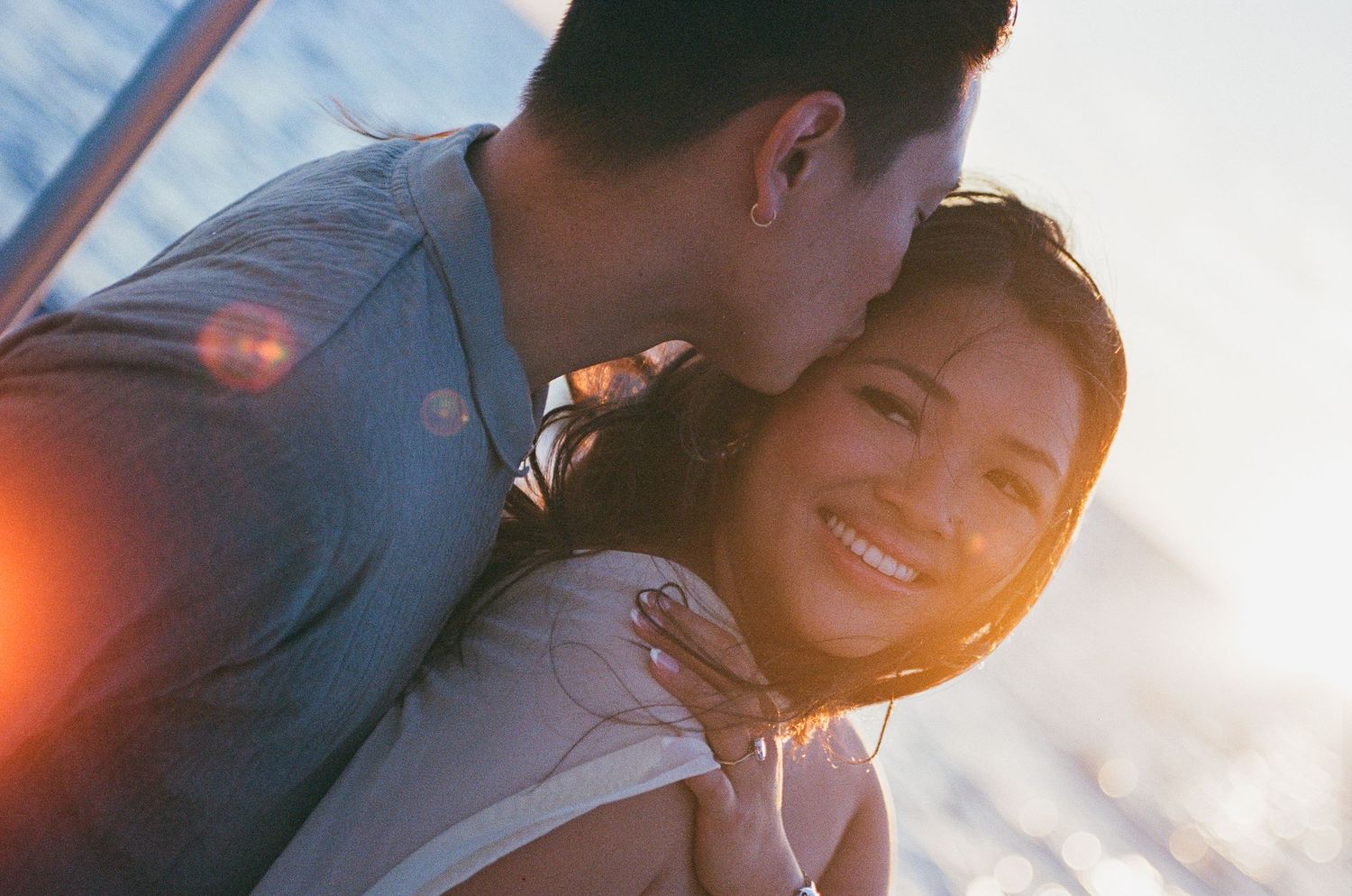 Couple sharing a romantic sunset moment, man kissing woman's cheek as she smiles joyfully with golden light behind them in Cabo San Lucas.
