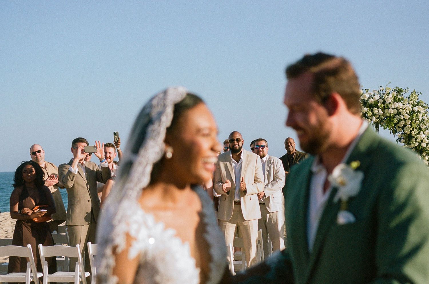 Newlyweds laughing after ceremony with photo focused on the guests smiling behind them.