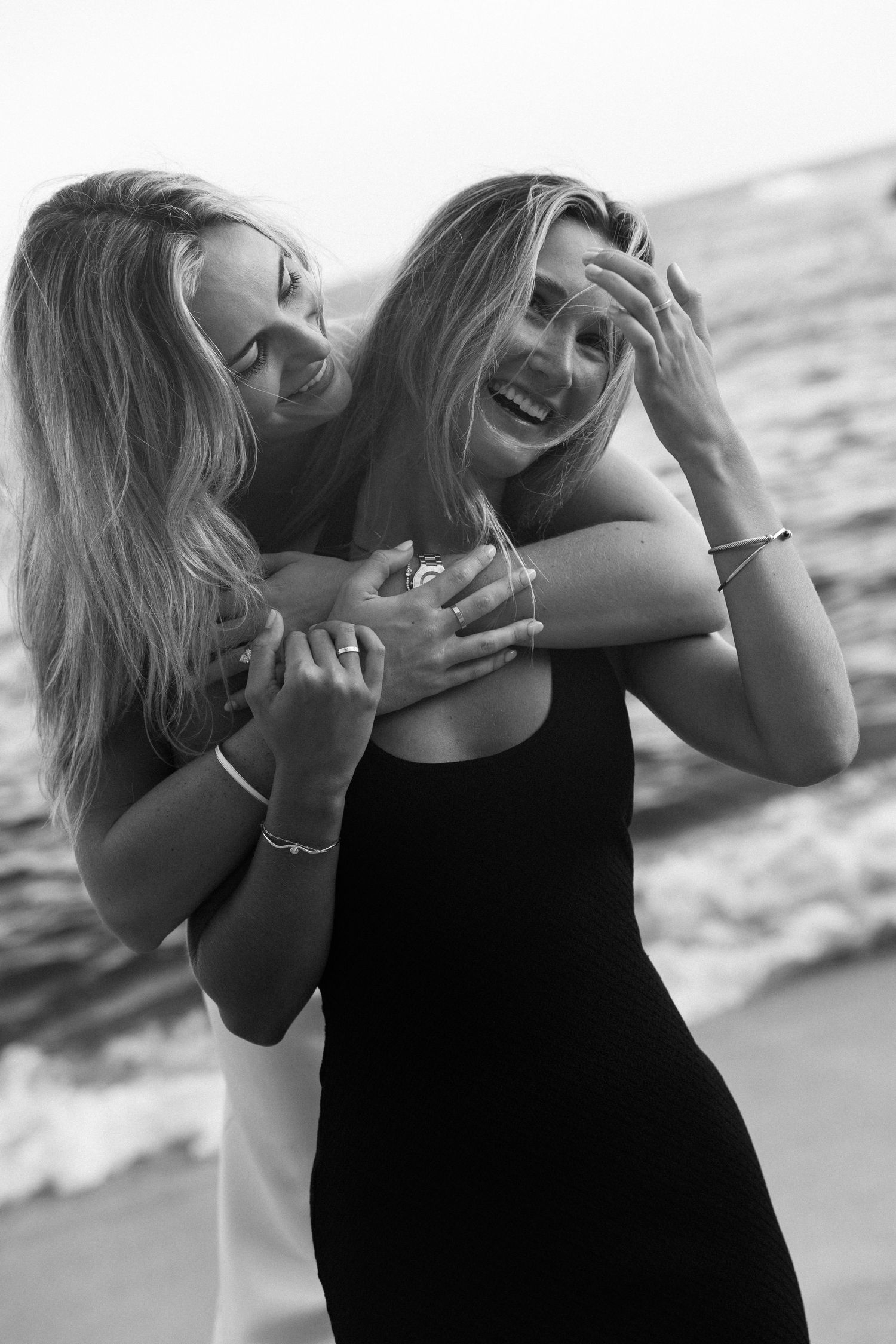 Two blonde women laughing and embracing on a beach in black and white photo.