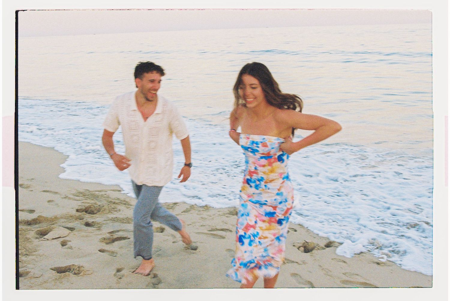 Newly engaged couple laughing running from waves on beach in San José del Cabo.
