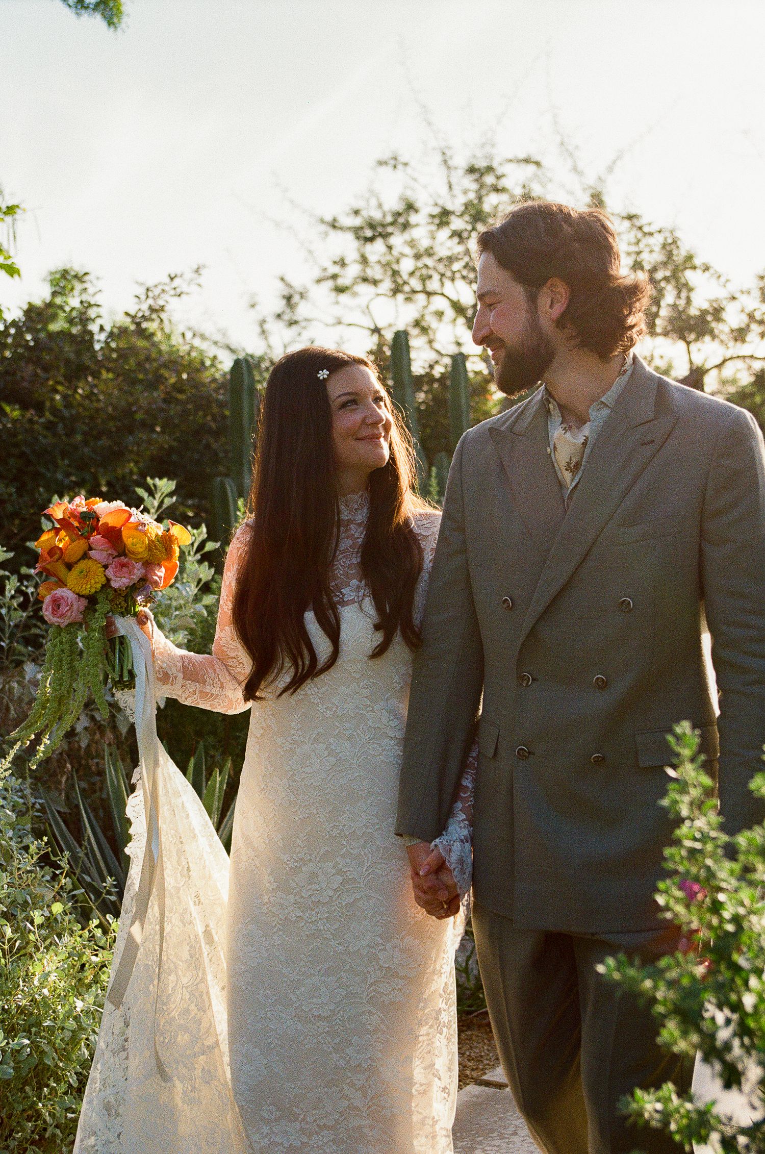 Newlyweds holding hands, looking at each other while walking up path at Acre Resort, Los Agaves.