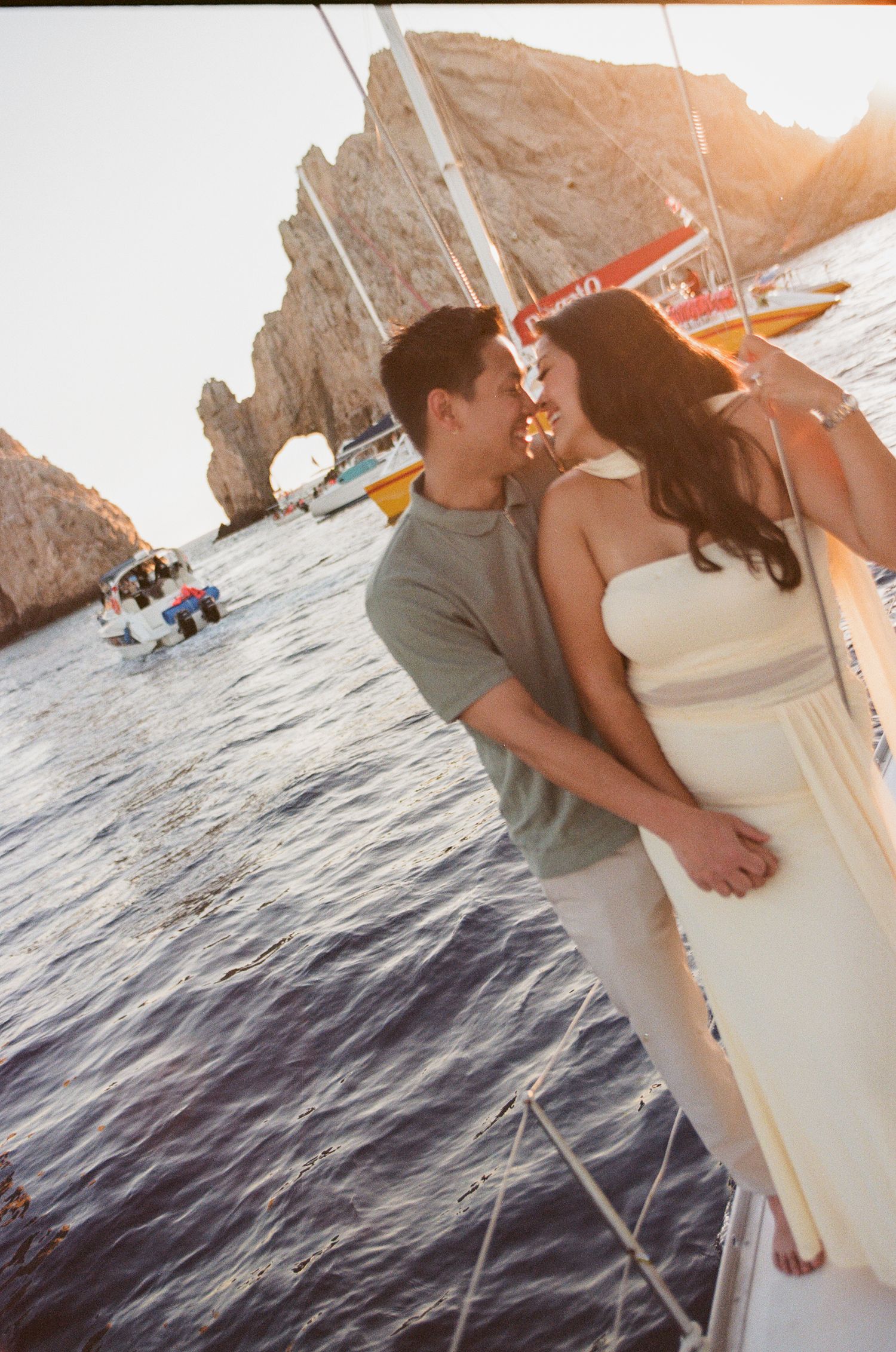 Couple sharing a romantic moment on a sailboat with scenic ocean rock arch and golden sunset in Cabo San Lucas, Mexico.